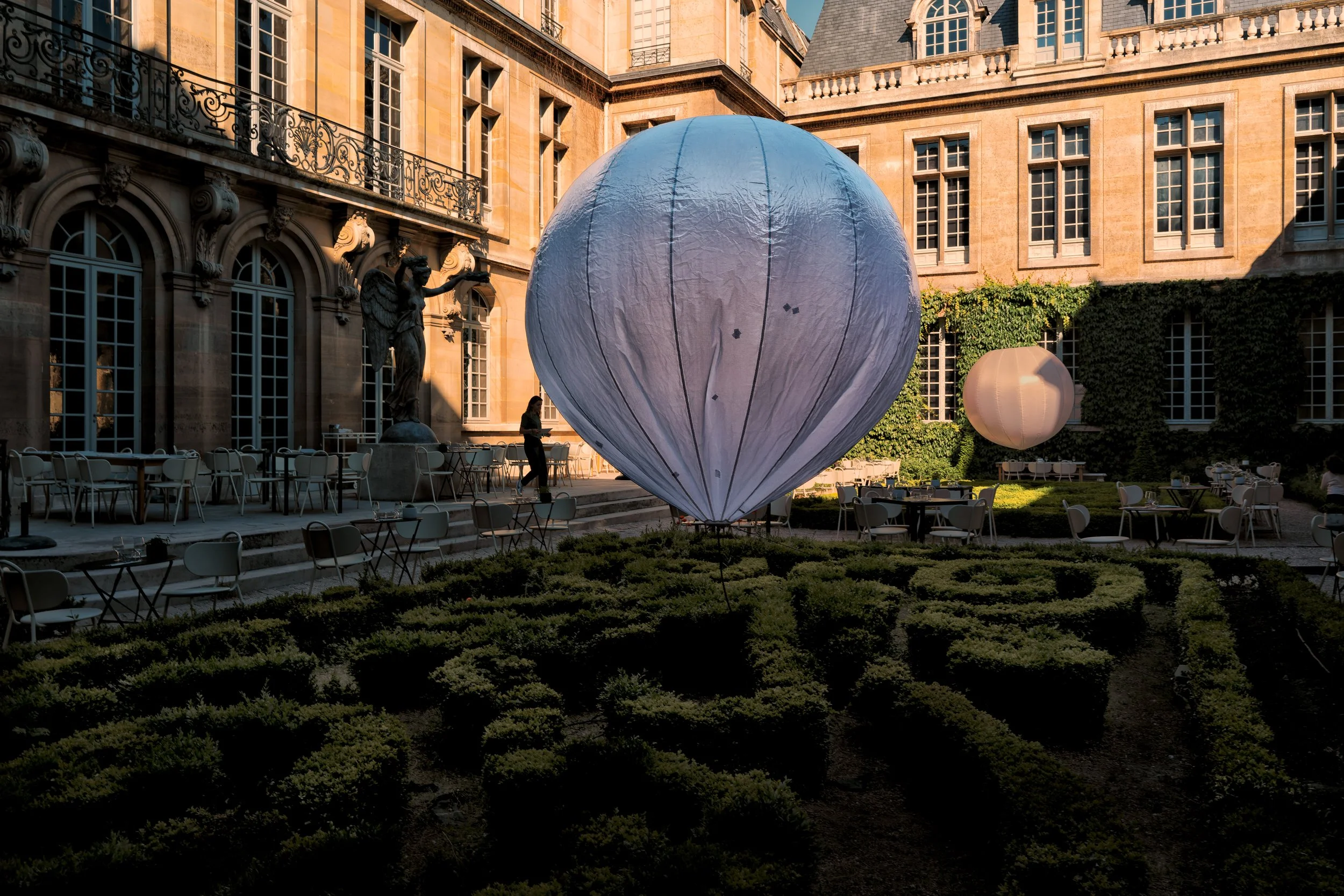 Between Stone and Air

Soft, suspended forms interrupt the measured order of a formal Parisian courtyard. Set against carved stone, clipped gardens, and repeating windows, they seem both weightless and monumental—temporary presences held between arch