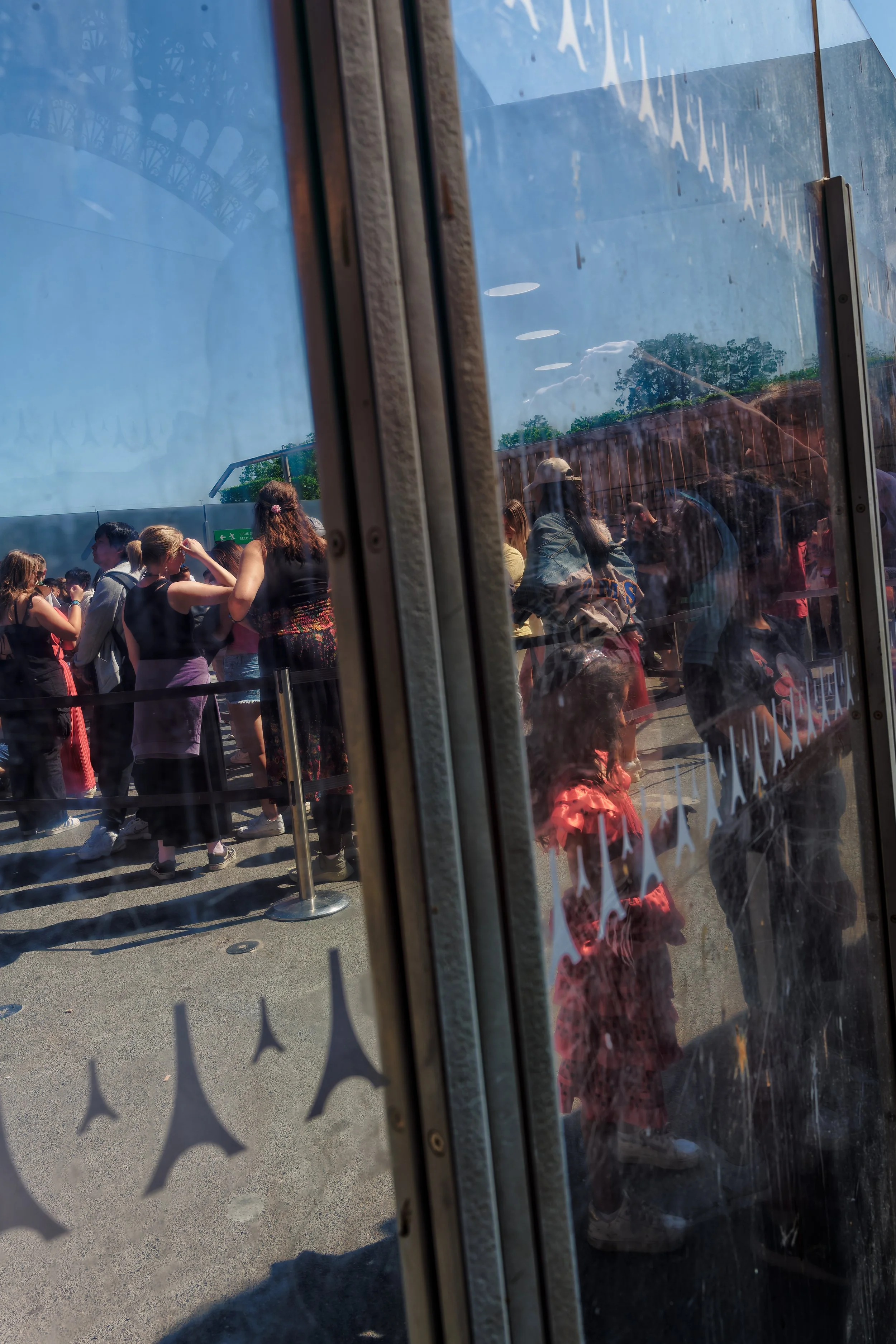 Paris street scene viewed through reflective glass, with a red-dressed figure, a crowd, repeated Eiffel Tower motifs, and a faint reflection of the Eiffel Tower.