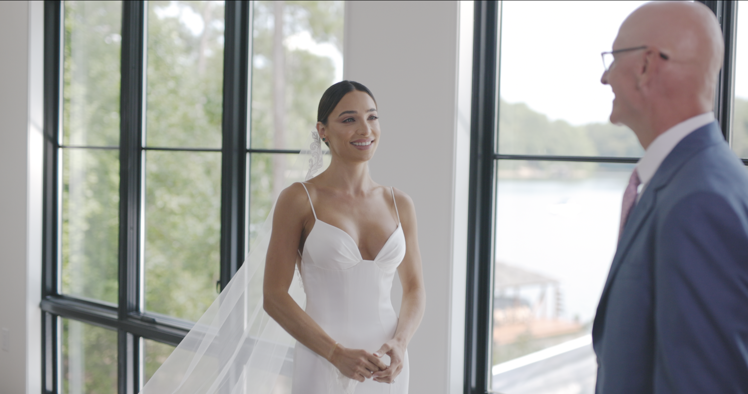 Bride smiling in a wedding dress beside her father by a lakeside window, wedding film still, Greenville SC