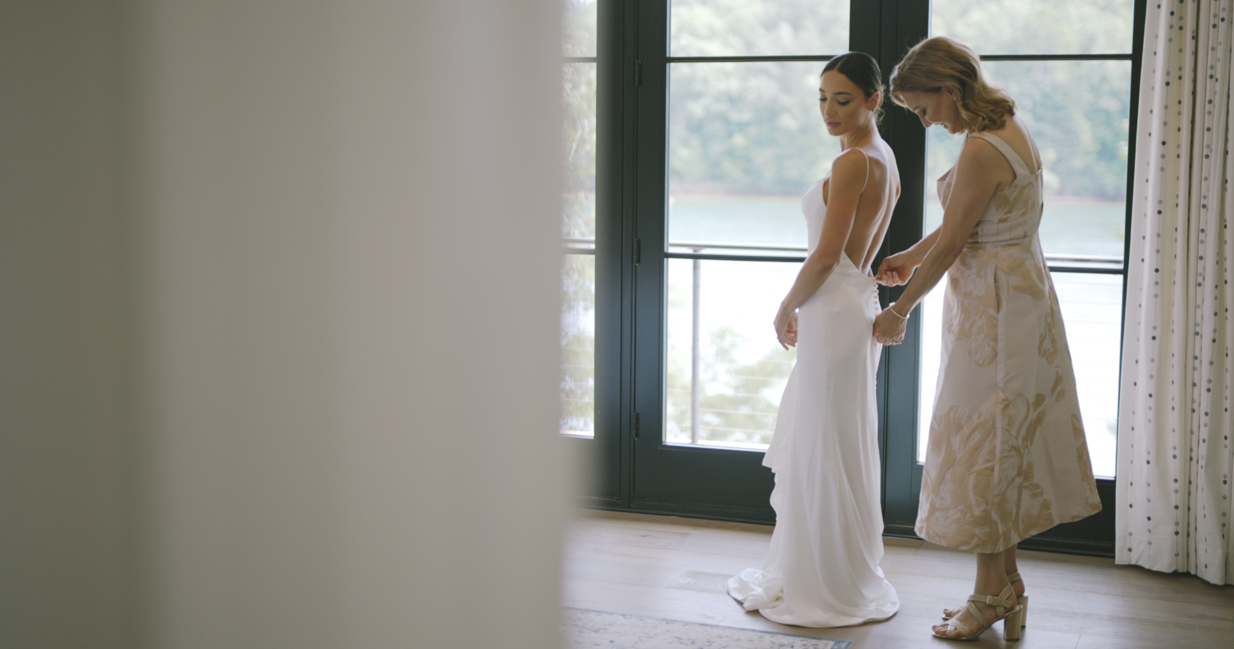 Bride in a wedding dress getting ready with help from a woman beside a window, wedding film still, Greenville SC