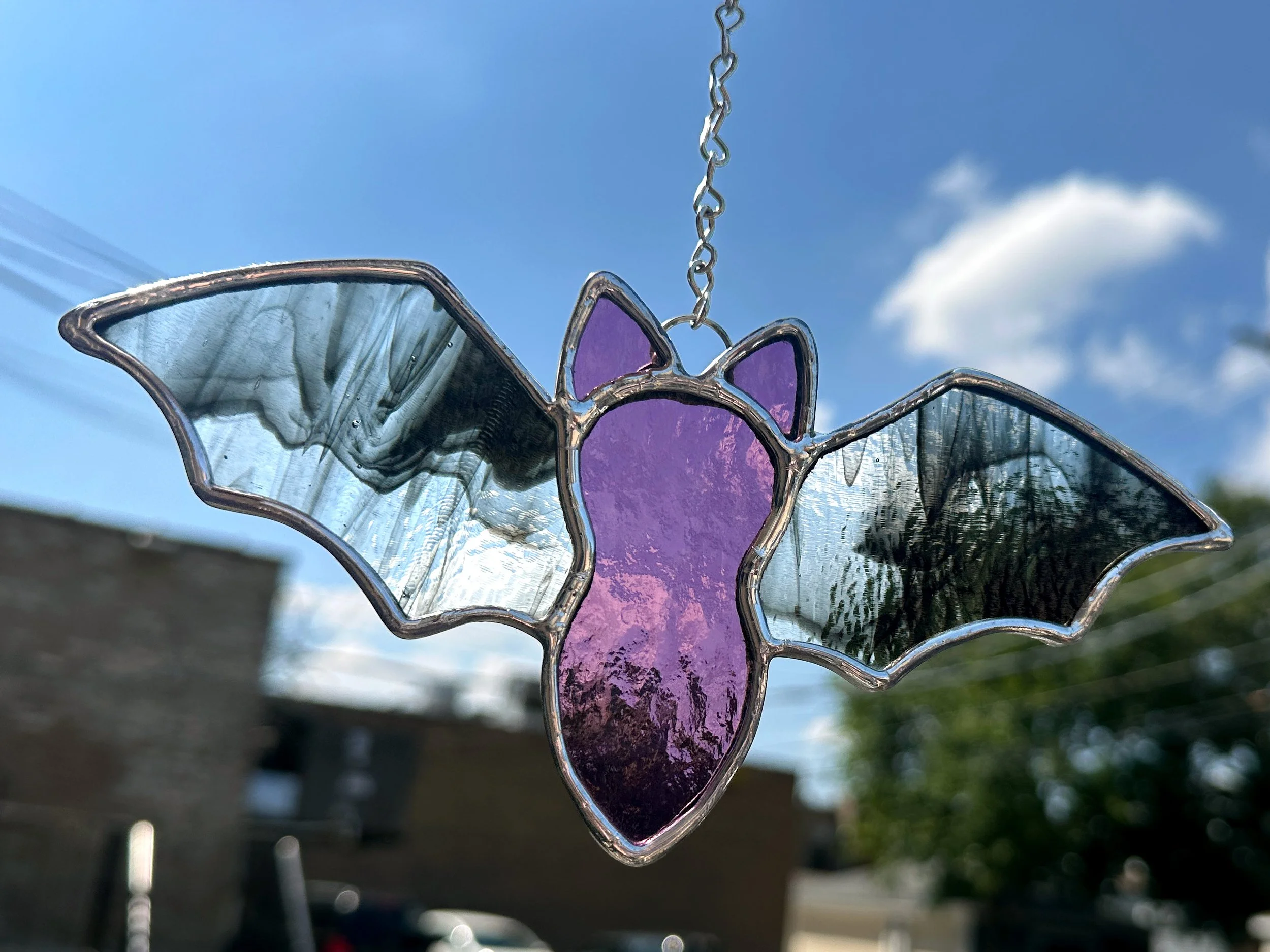stained glass sun catcher bat with a purple body and beautiful streaky black and clear wings. Hanging in the sunlight shining with beautiful color. example for make your own stained glass class called glass in a flash at stern glass works