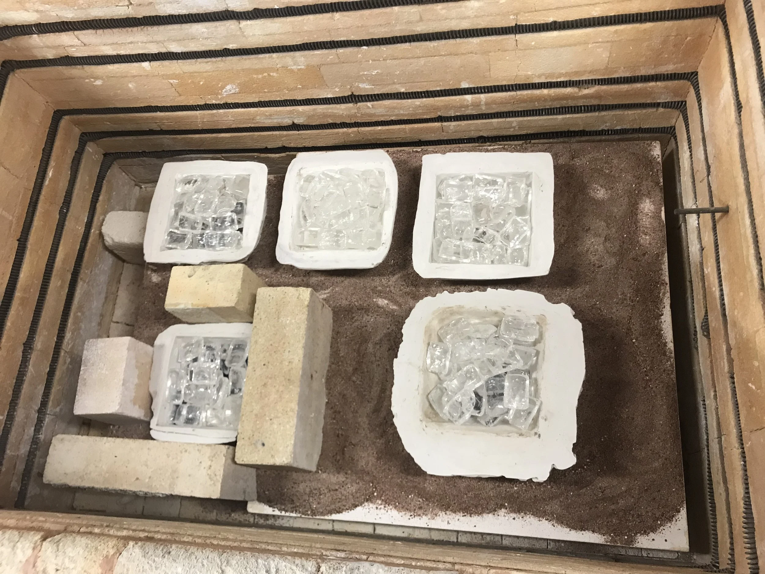a group of three friends working side by side on a fused glass project in a small group lesson. You can see them carefully laying out their materials to create fused glass trays