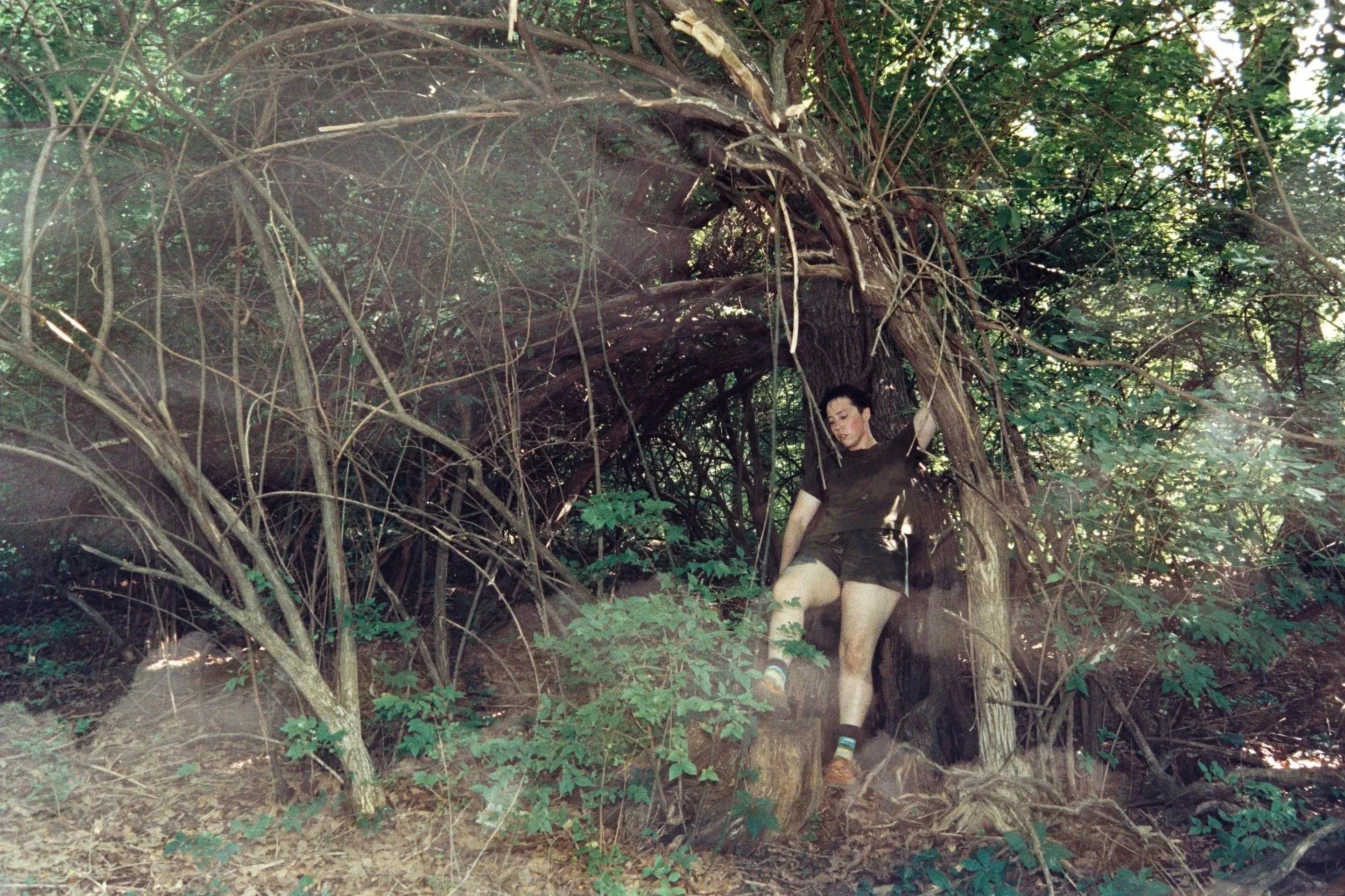 A color double-exposure self-portrait shows a figure leaning against a tree in the woods, with clouds lightly layered across the image.