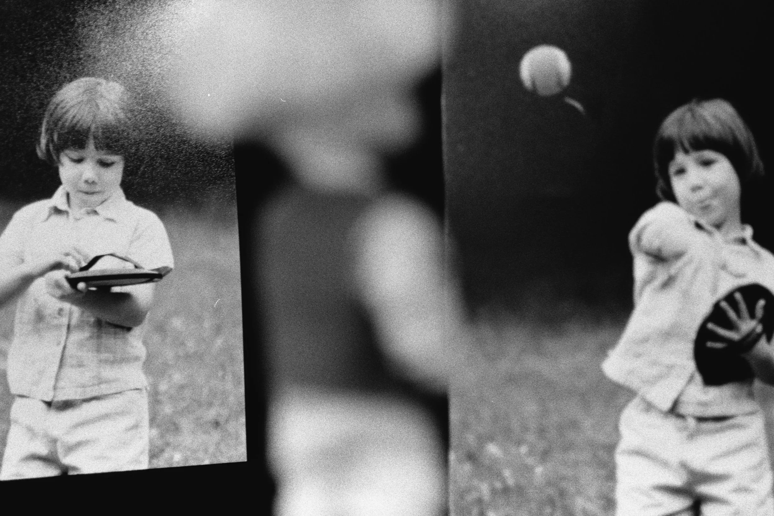 A black-and-white photo shows two childhood photos against a black backdrop, with an out-of-focus Tommy doll in the foreground.