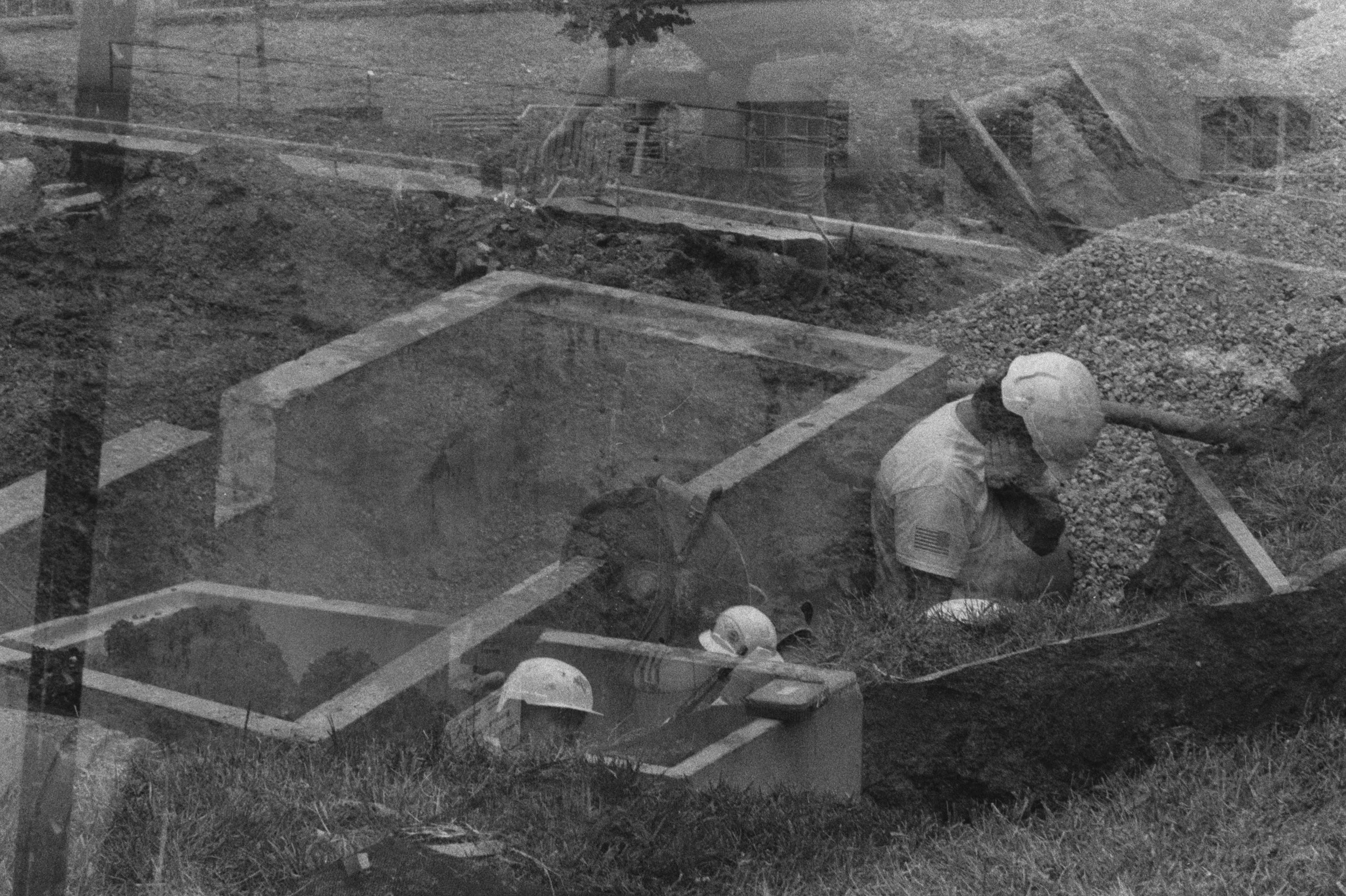 A black-and-white double exposure shows three workers digging trenches, two partly buried in Dubuque Street and one covering his face behind them.