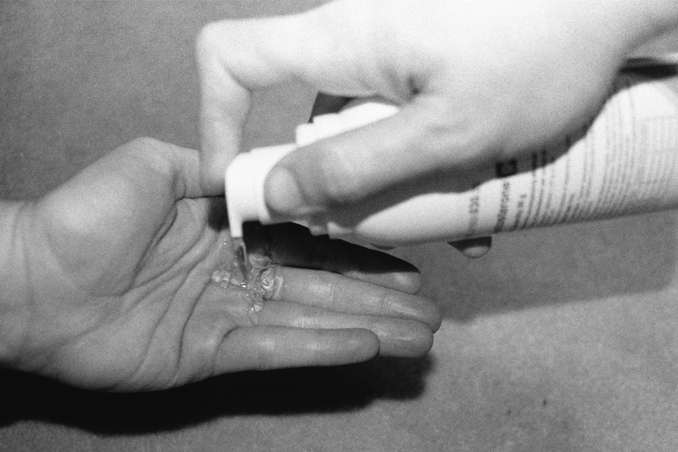 A black-and-white flash photo shows testosterone gel being dispensed from the right hand into the left palm.
