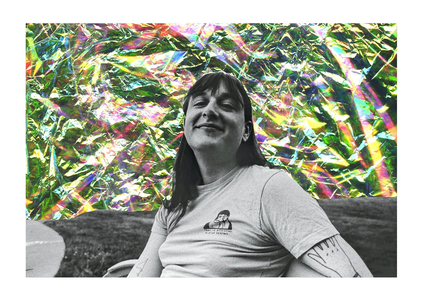 A black-and-white portrait shows a white trans woman smiling on a park bench, with grass behind her and pink-gold iridescent cellophane in the sky.