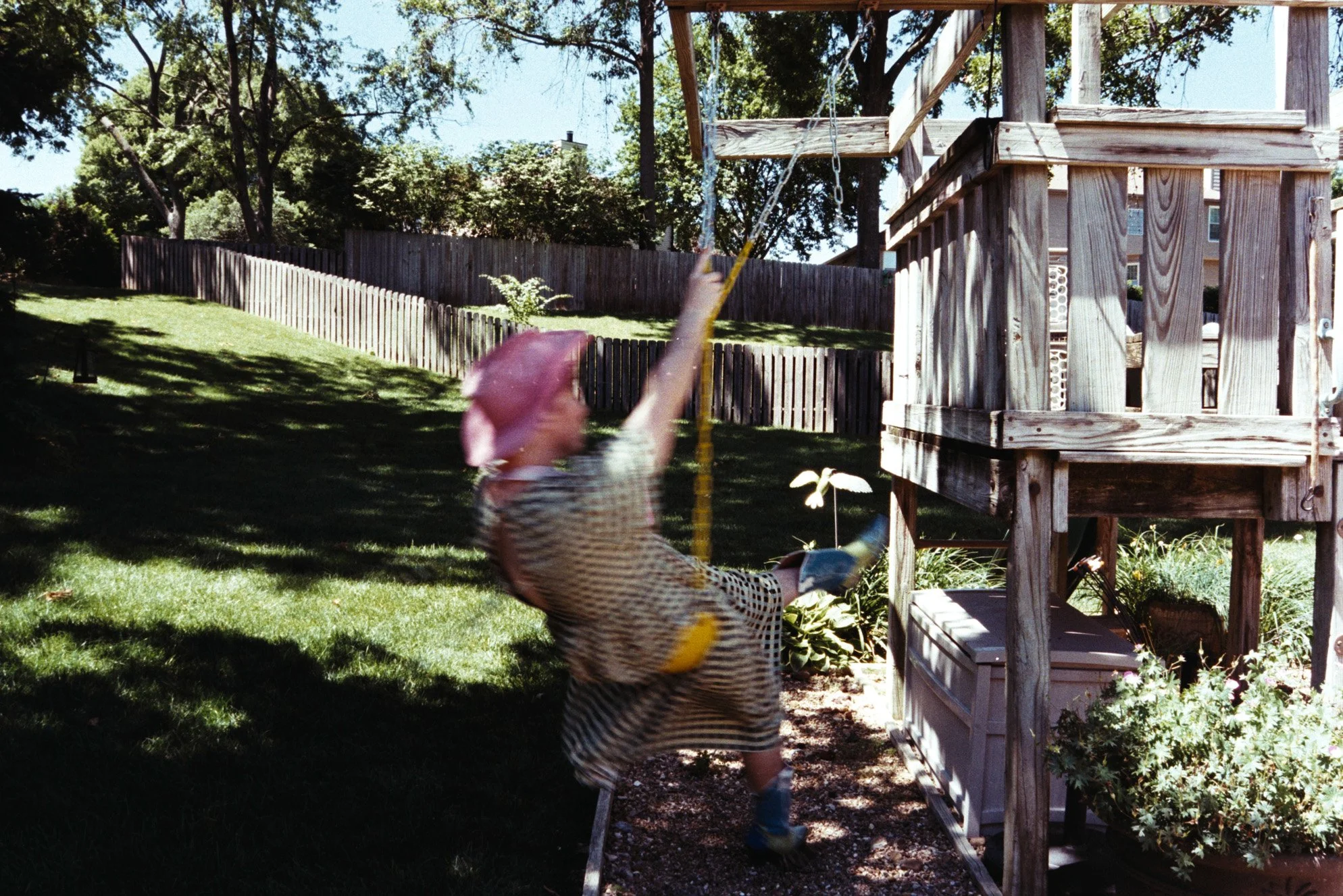A blurred self-portrait shows a figure twirling on a childhood swing set, wearing a pink cowboy hat, checkered dress, and blue-green boots.
