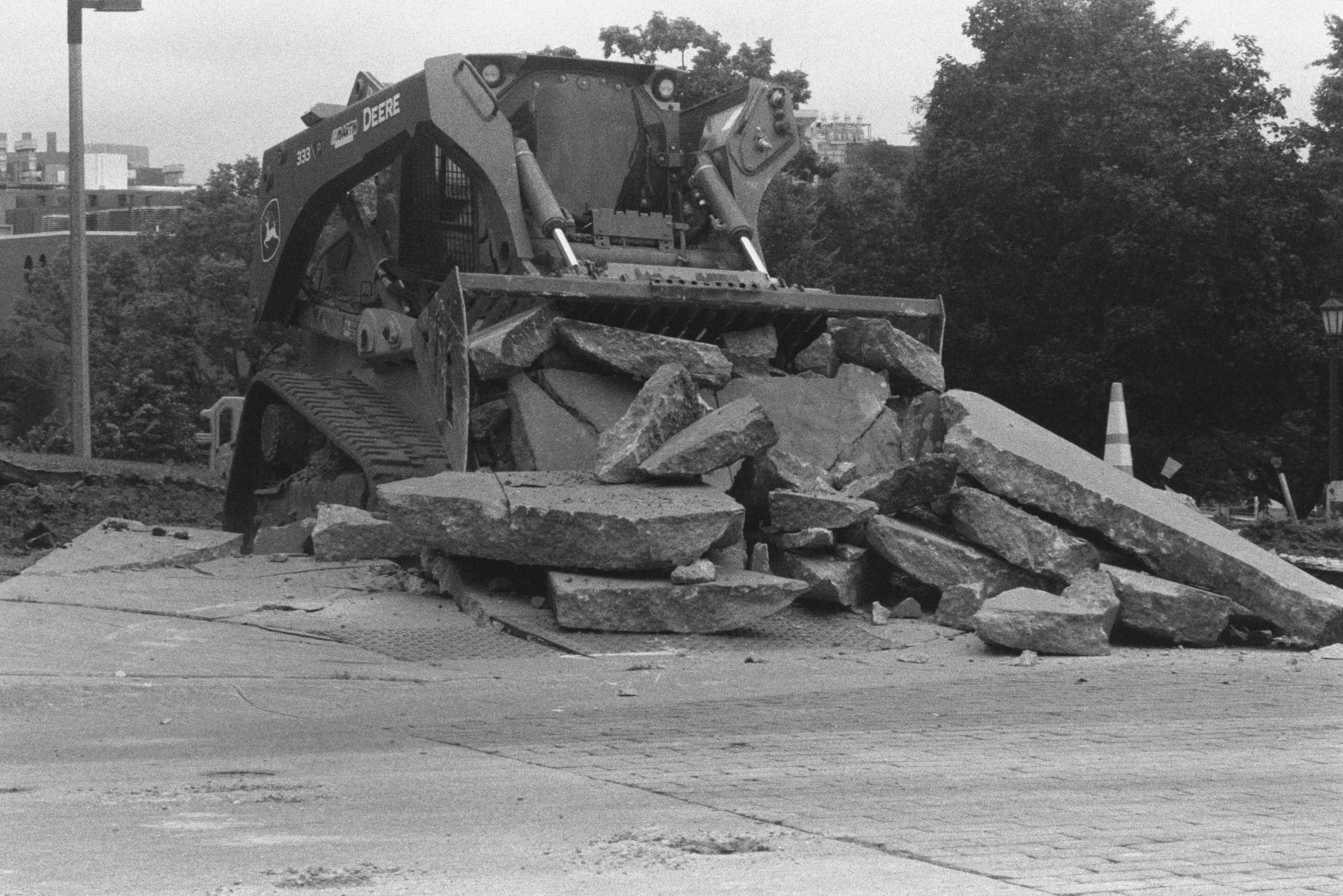 A John Deere skid steer pushes broken concrete slabs across Dubuque Street.