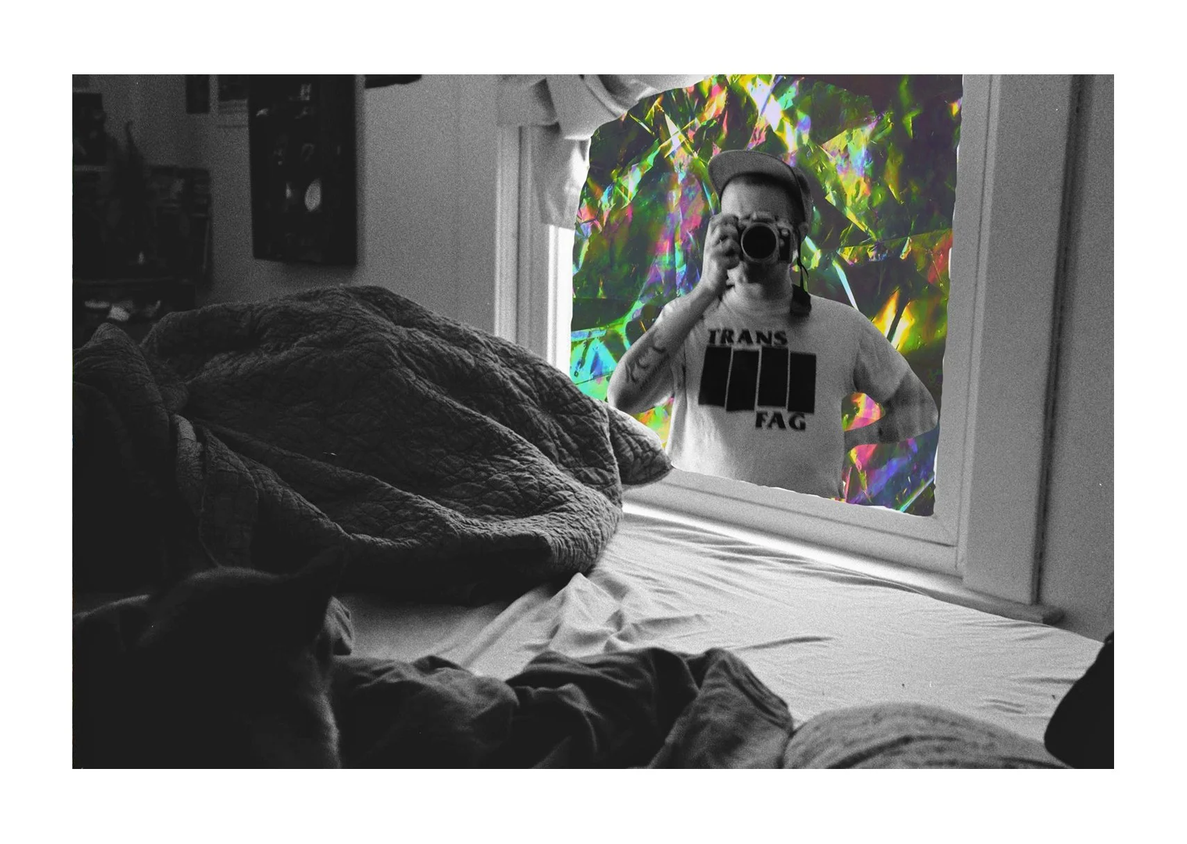 A black-and-white photo shows an unmade bed with a cat in the corner and a window collage of a person in a “TRANS FAG” shirt holding a camera.