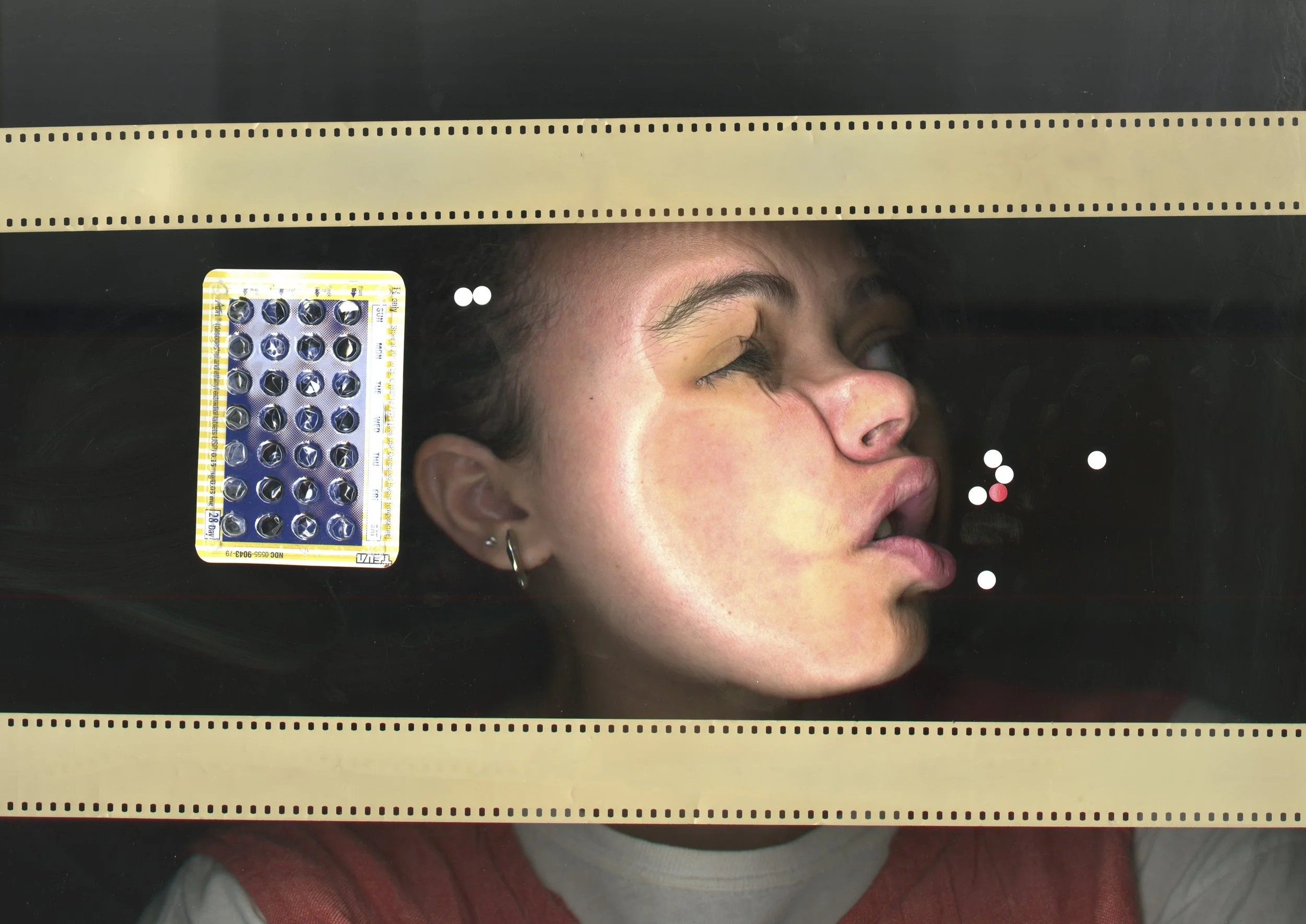 Pensée’s face presses against a scanner, distorted beside a birth control packet and scattered pills, framed by film strips in an imagined MRI setting.