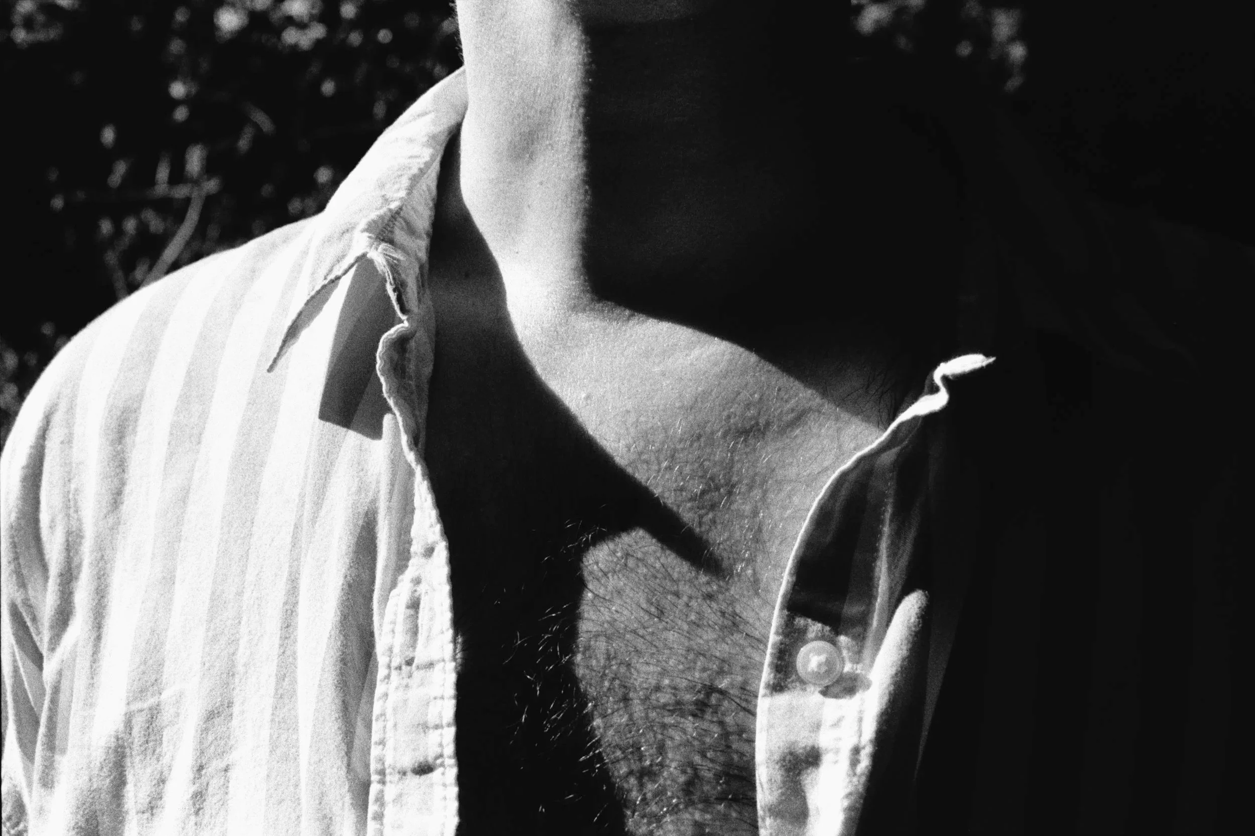 A black-and-white photo of a chest and neck in an open striped shirt, with chest hair lit beneath the collar’s shadow.