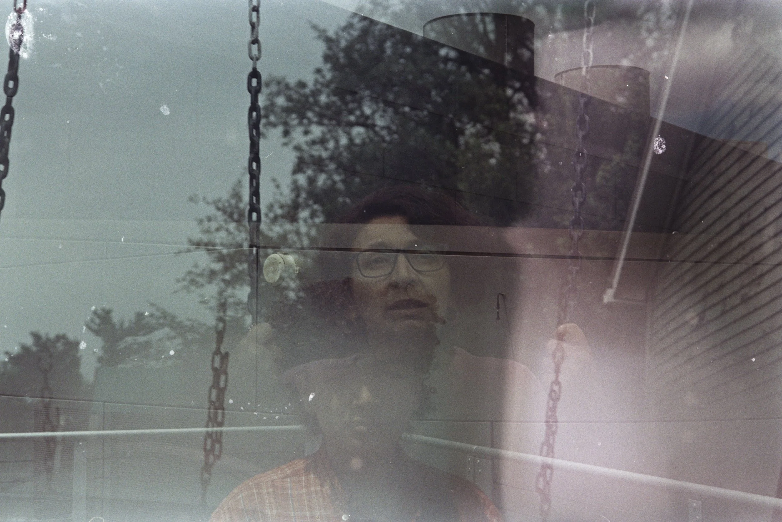 A double exposure shows a woman with short wavy hair and glasses on a garden swing, layered with trees and Pensée looking at the camera from a rooftop.
