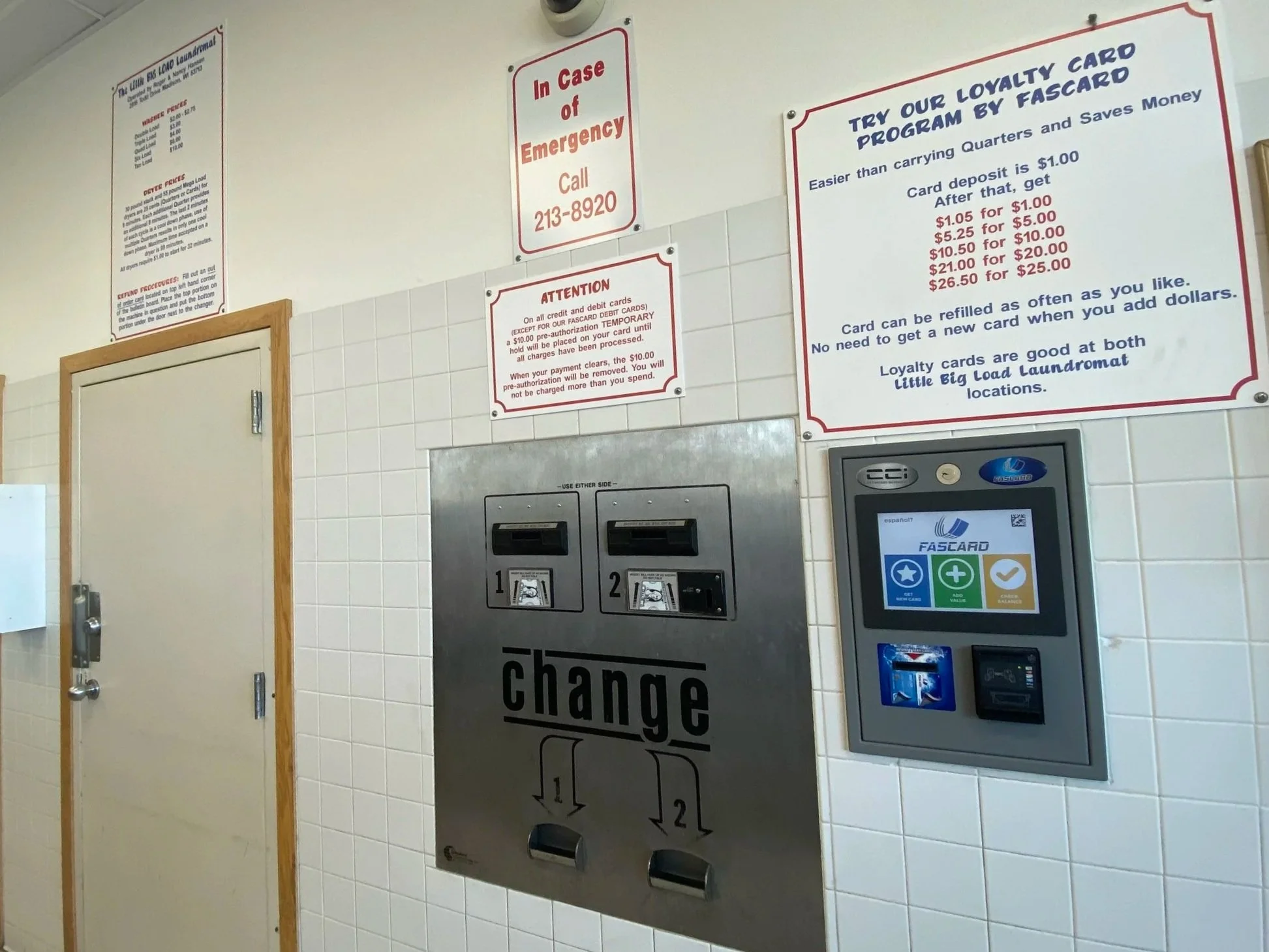 Laundromat wall with card reader, change machines, and informational signs about loyalty card program and emergency contact.