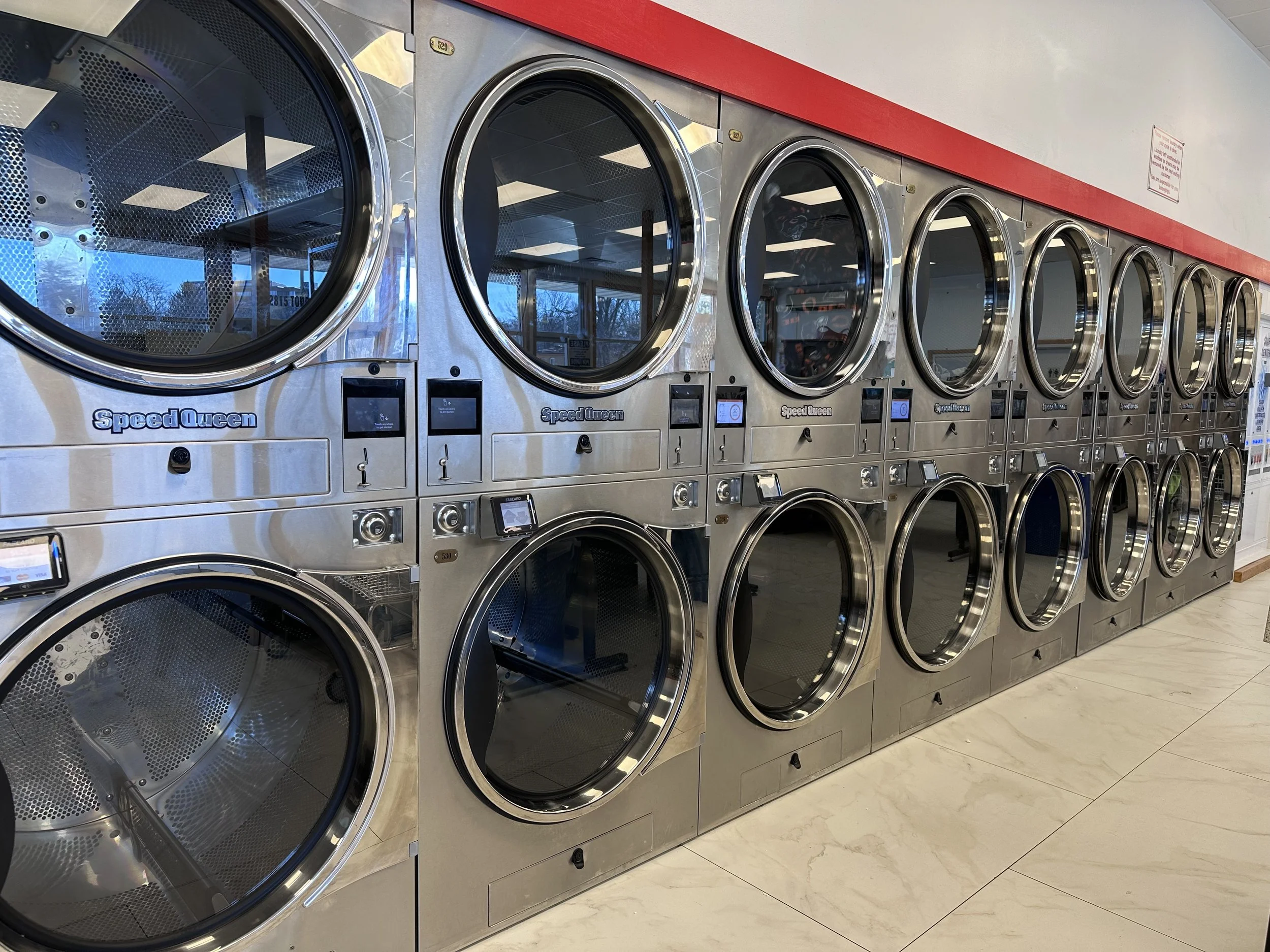 Row of stainless steel commercial washers in a laundromat with round glass doors and digital controls.