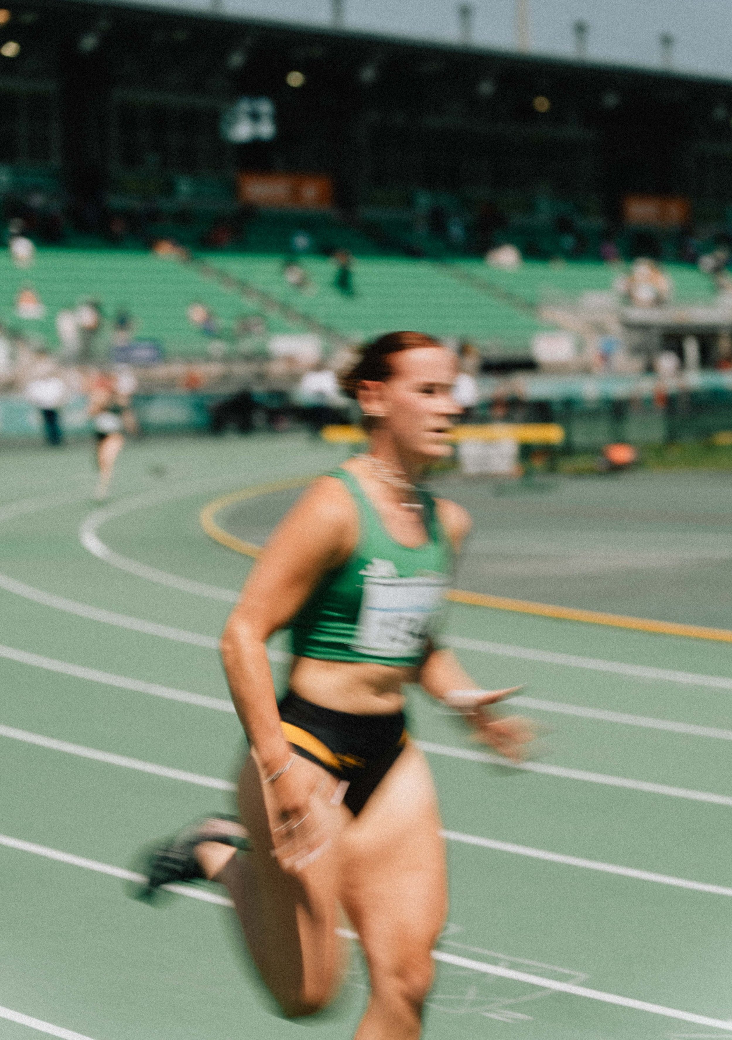 Une femme court sur une piste d'athlétisme en compétition, avec un public dans les gradins en arrière-plan.