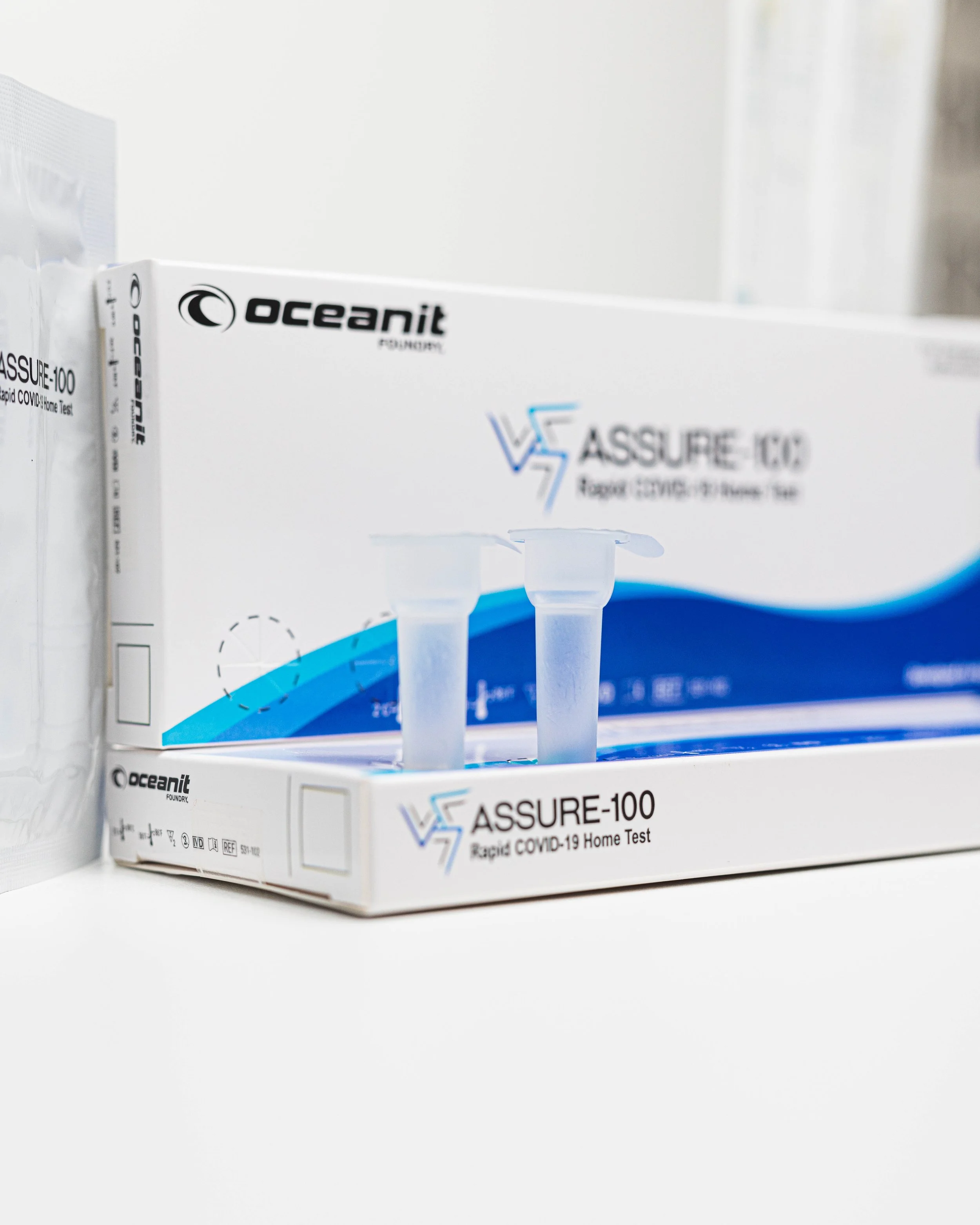 A box of Oceanit Assure-100 rapid COVID-19 home test kits on a white surface.