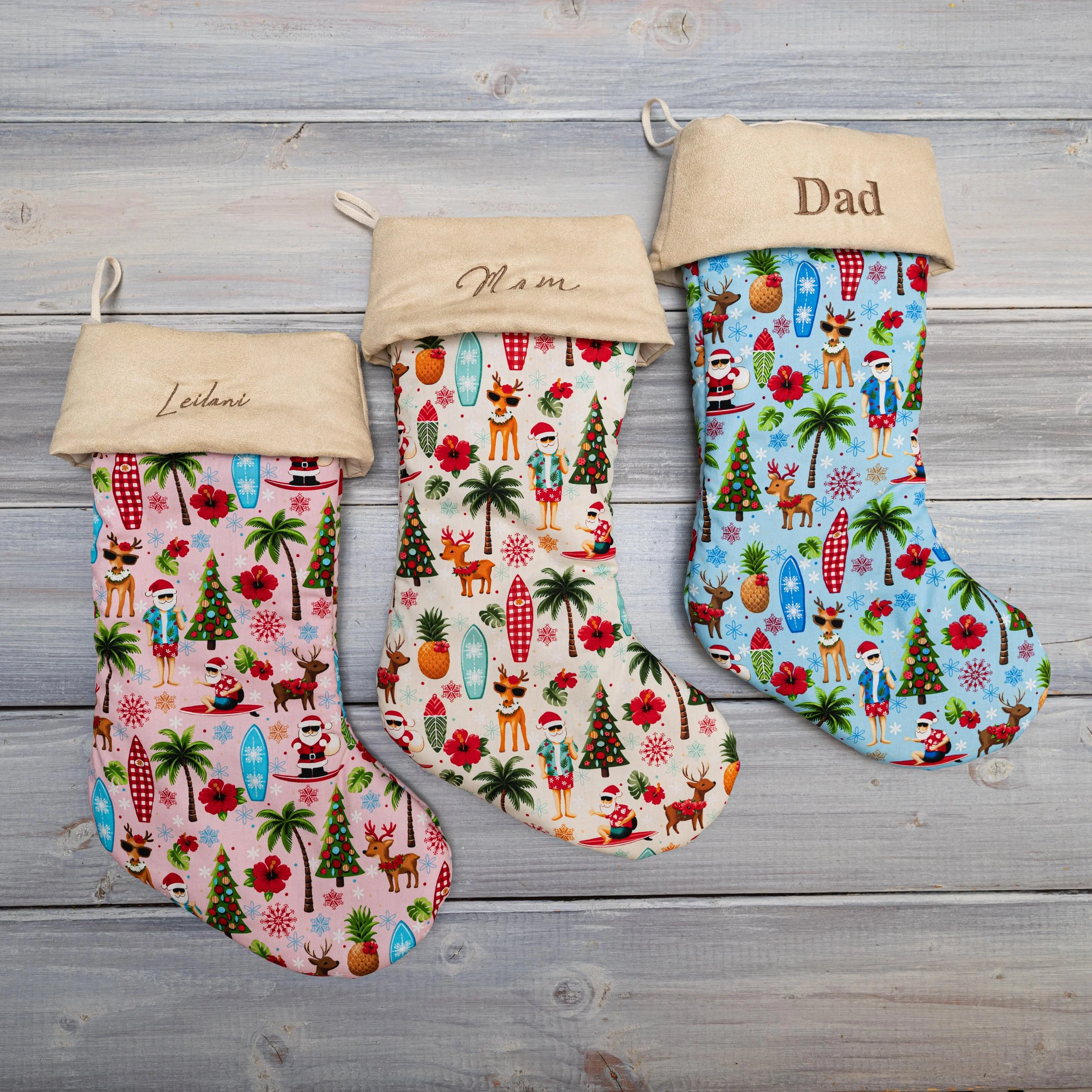 Three Christmas stockings with cartoon holiday characters and patterns hanging on a wooden surface, with labels 'Leilani,' 'Mam,' and 'Dad' embroidered on the cuffs.