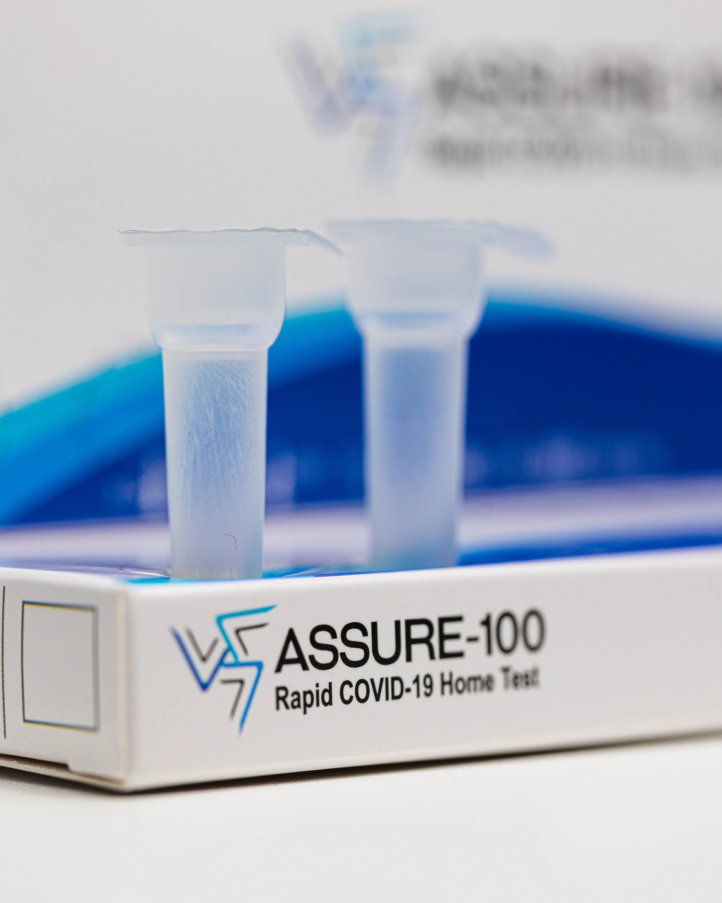 Close-up of a box of ASSURE-100 Rapid COVID-19 Home Test, showing the product name and logo, with a blurred background.