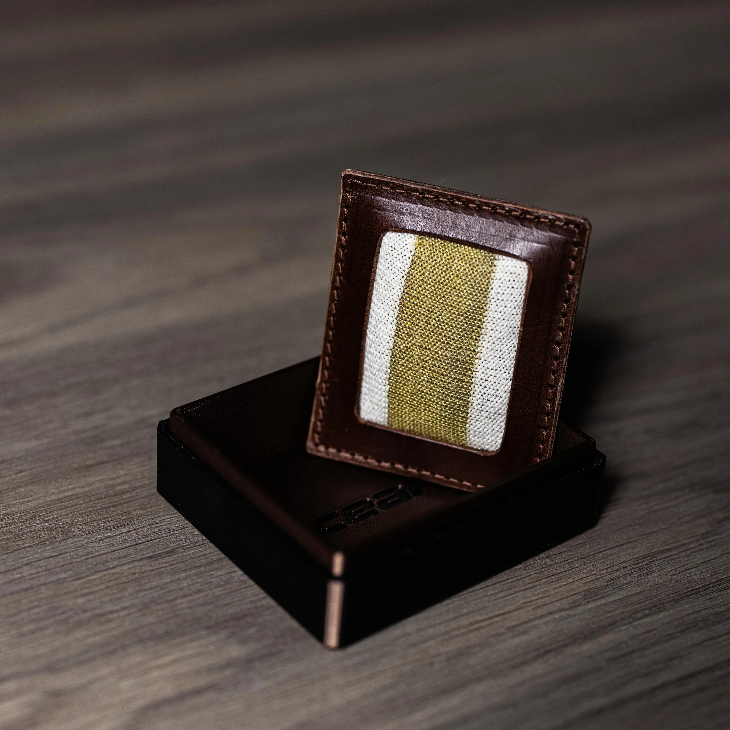 Close-up of a rectangular leather wallet with a fabric insert, displayed on a dark stand on a wooden surface.