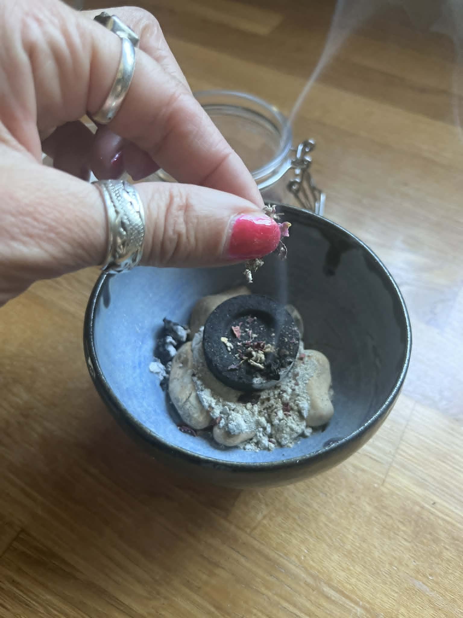 Loose incense being dropped onto a charcoal disc in a vessel