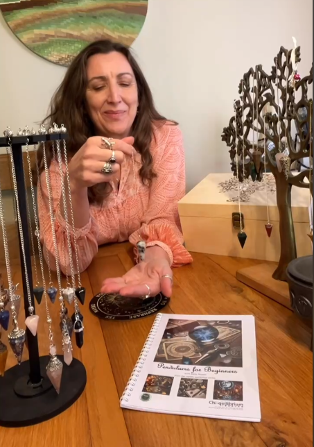 Kerry holding a pendulum with her Pendulums for Beginners workbook in the foreground.