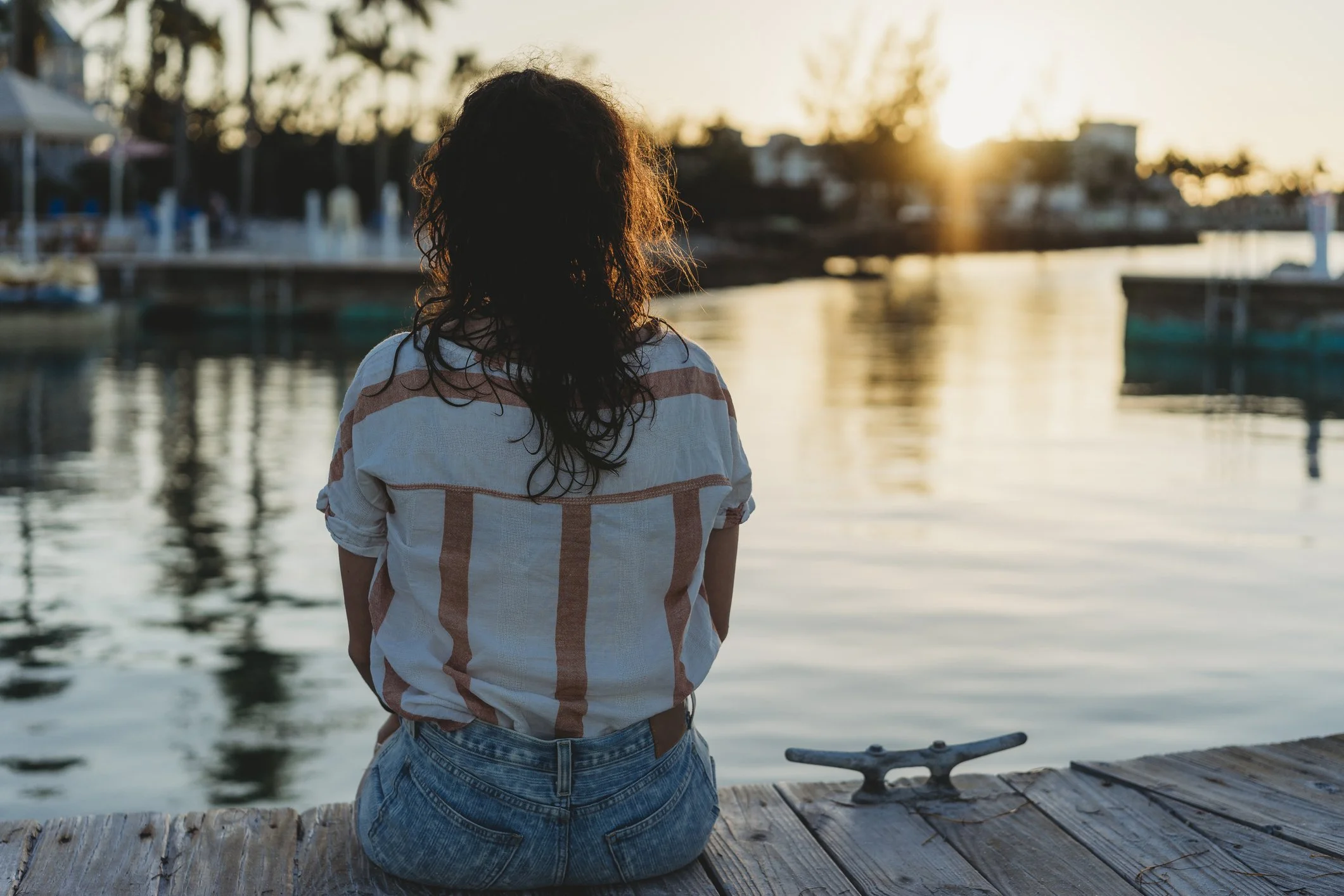 Woman sitting on dock, facing the sunset