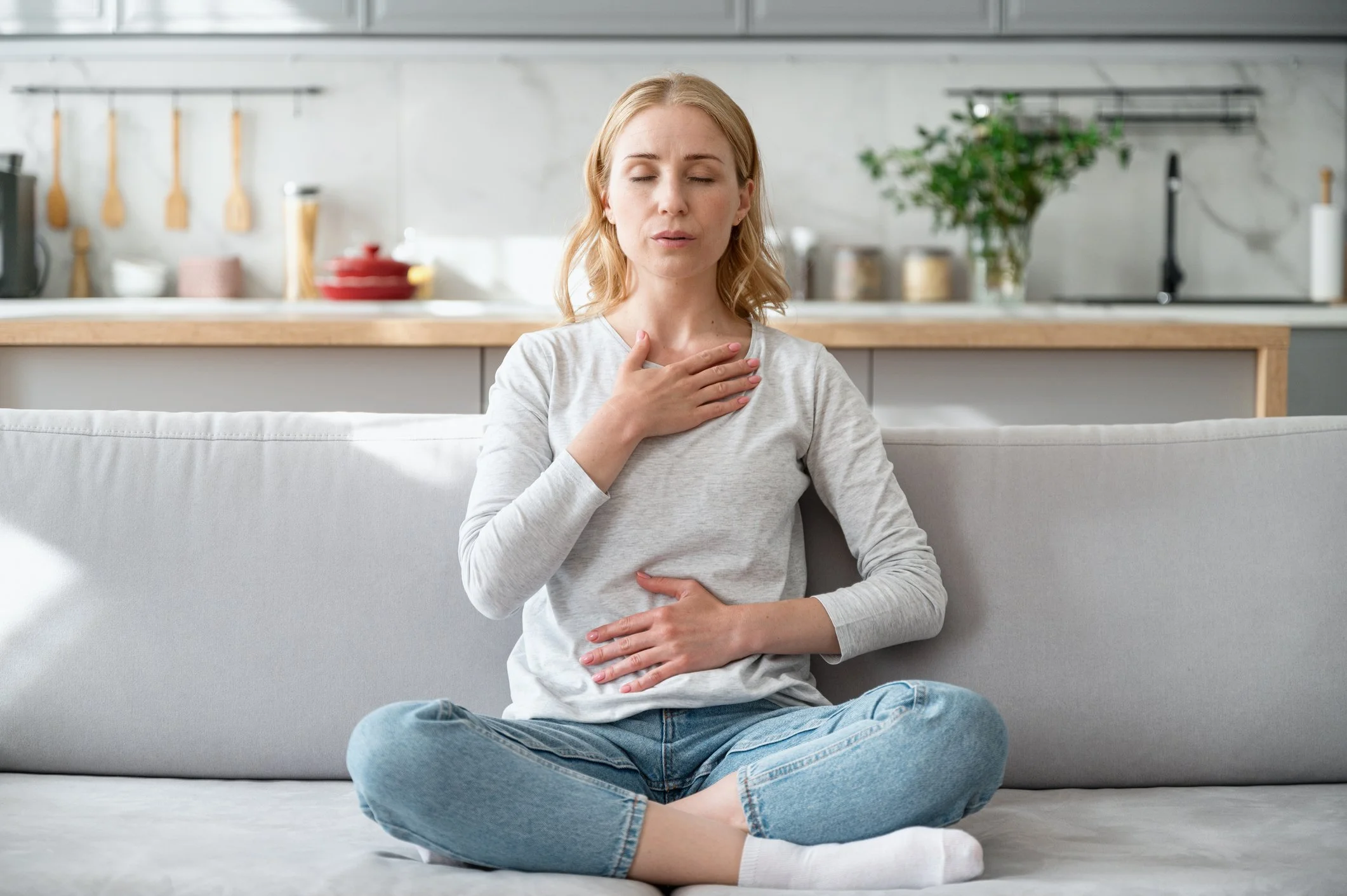 Woman sitting on couch with hand on heart and hand on belly
