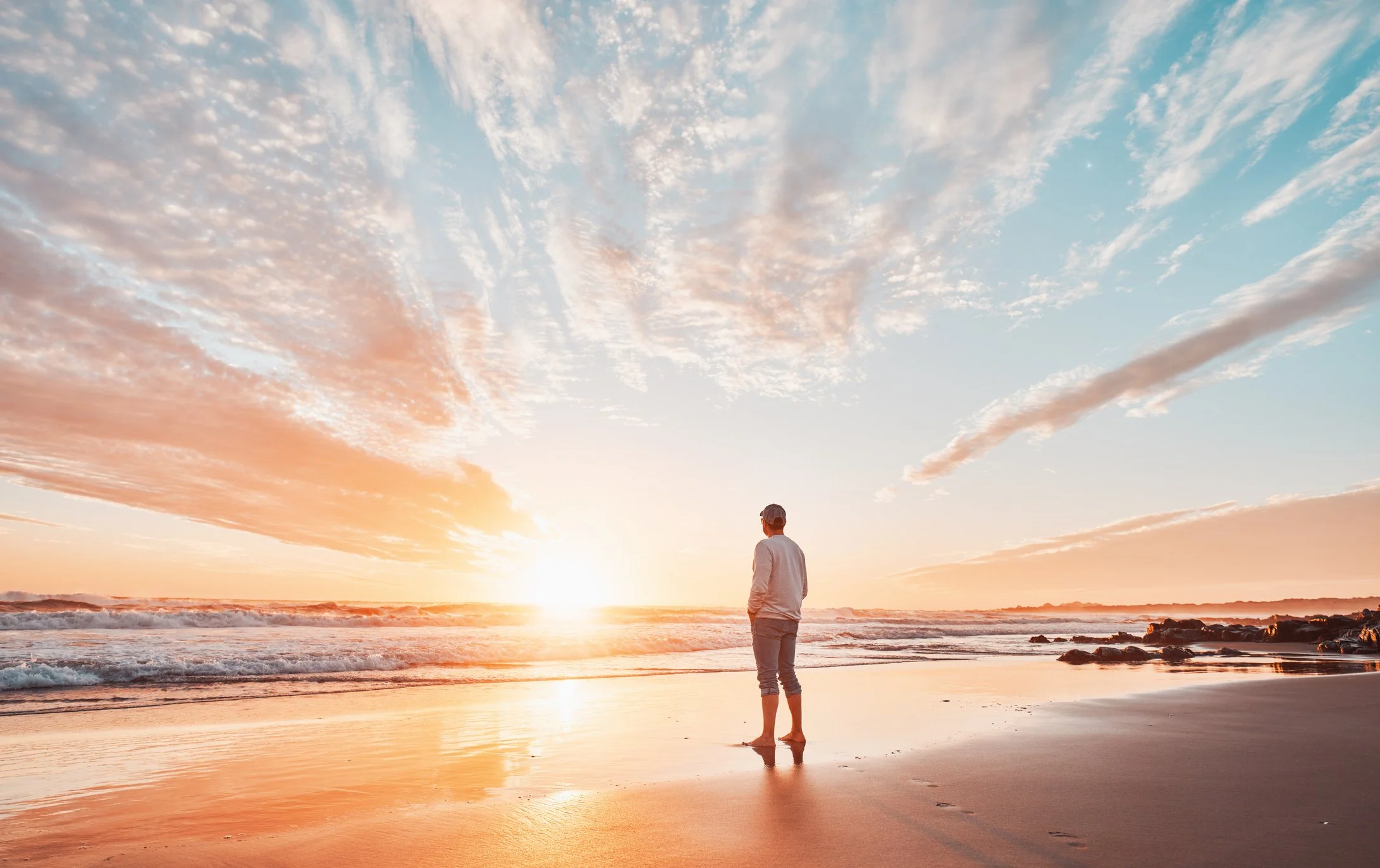 Man standing on the beach at sunrise looking out at the ocean.