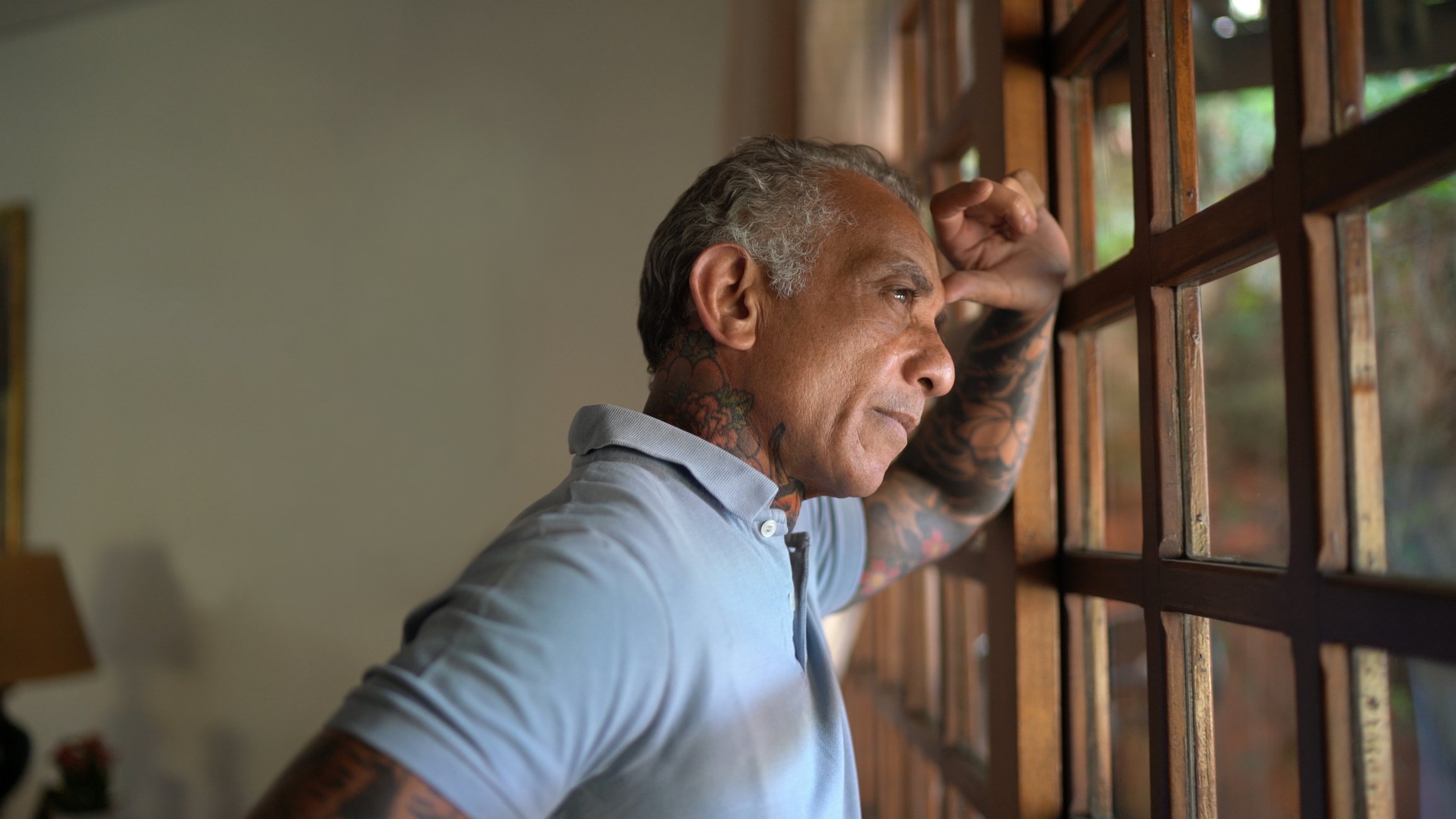 Man standing at the window looking outside resting his forehead in his hand and his hand on the window