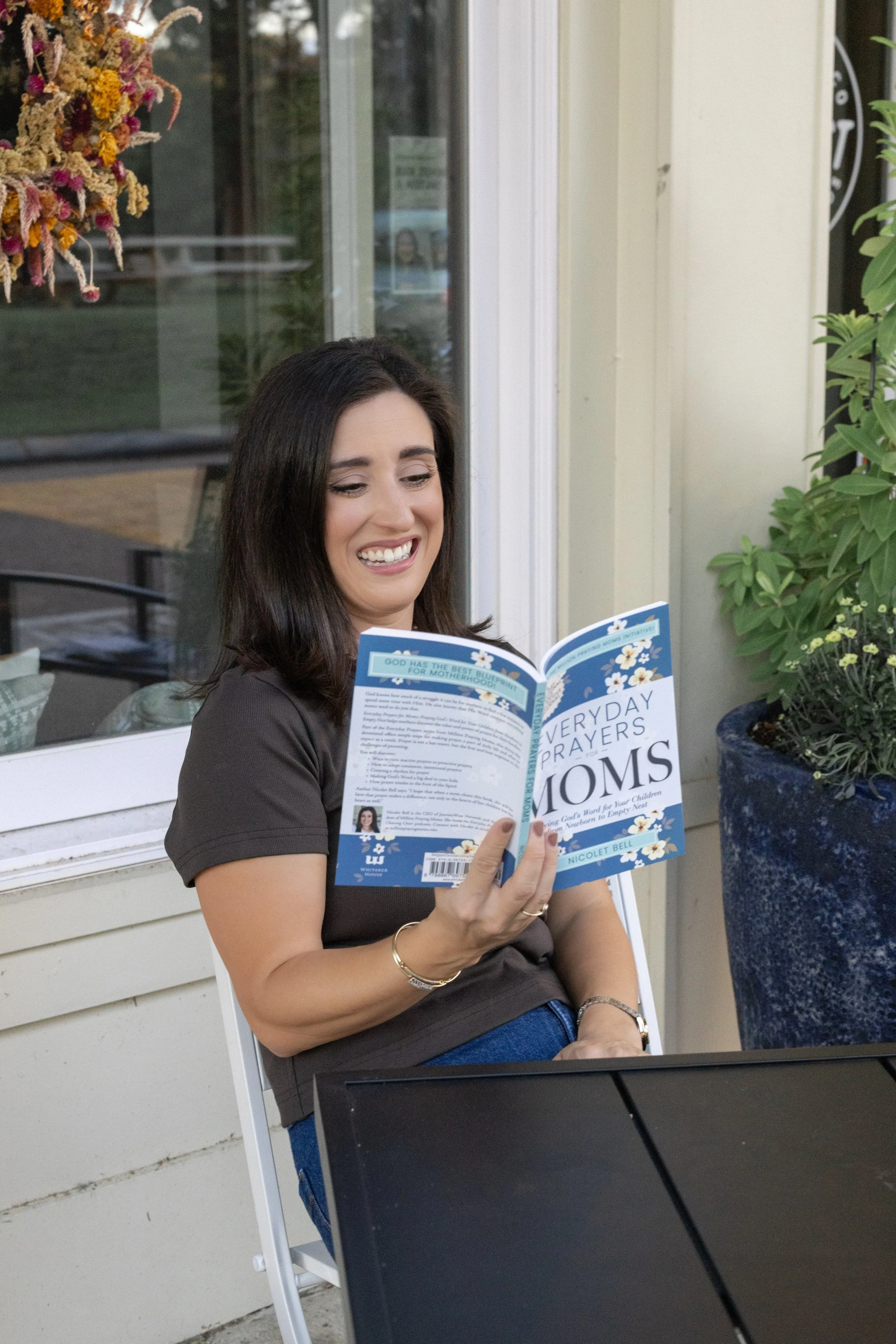 Nicolet Bell sitting at a table, laughing while reading the book Everyday Prayers for Moms.