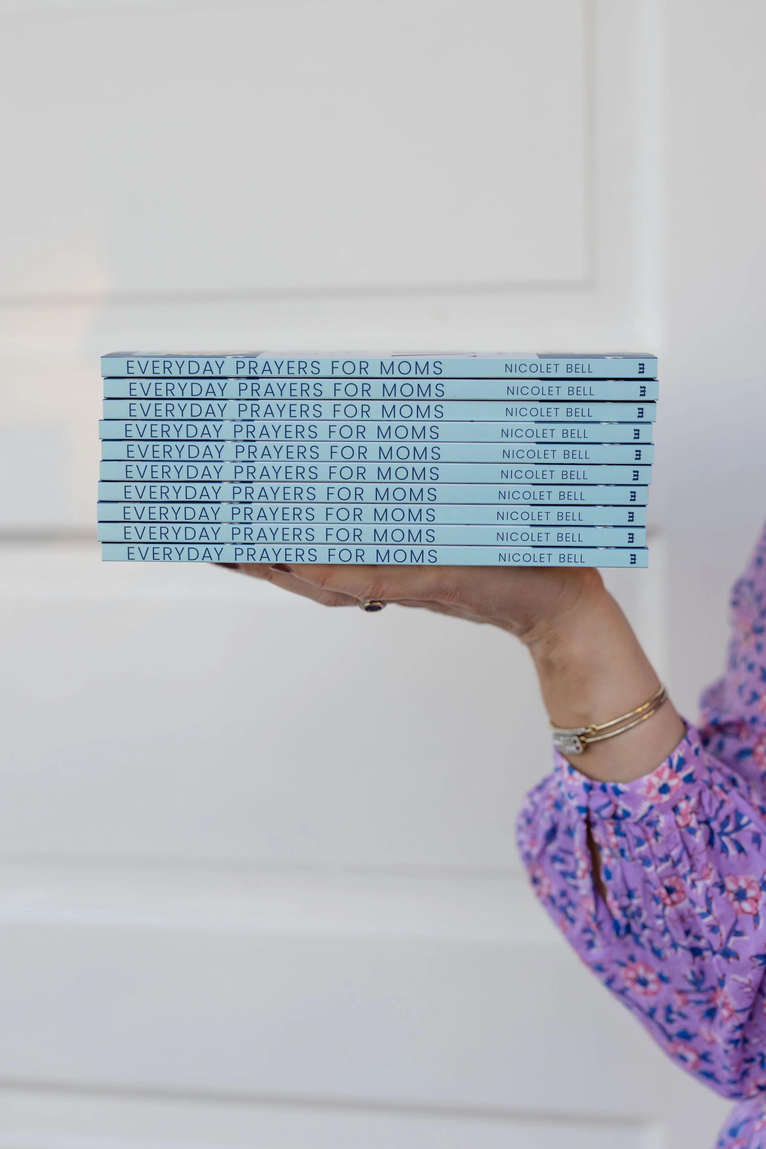 Nicolet Bell's arm holding a stack of books titled Everyday Prayers for Moms.
