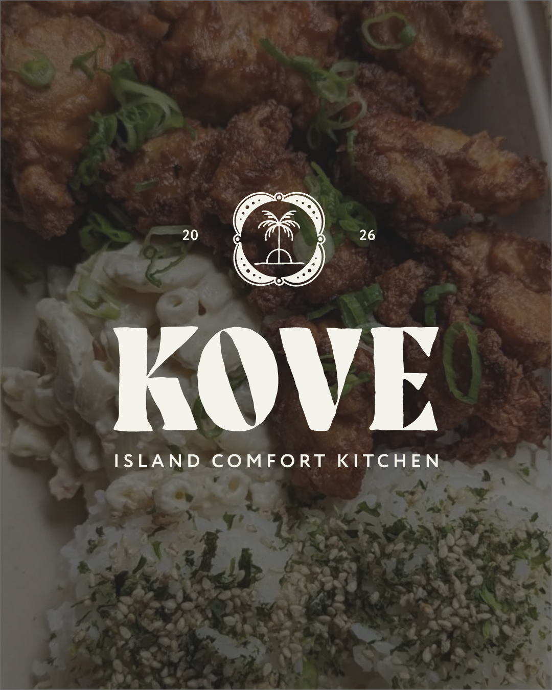 Close-up of fried chicken wings garnished with green onions, with macaroni salad and rice with seaweed and sesame seeds in the foreground, on a plate from Kove Island Comfort Kitchen, with a logo featuring a palm tree and the date 2026.