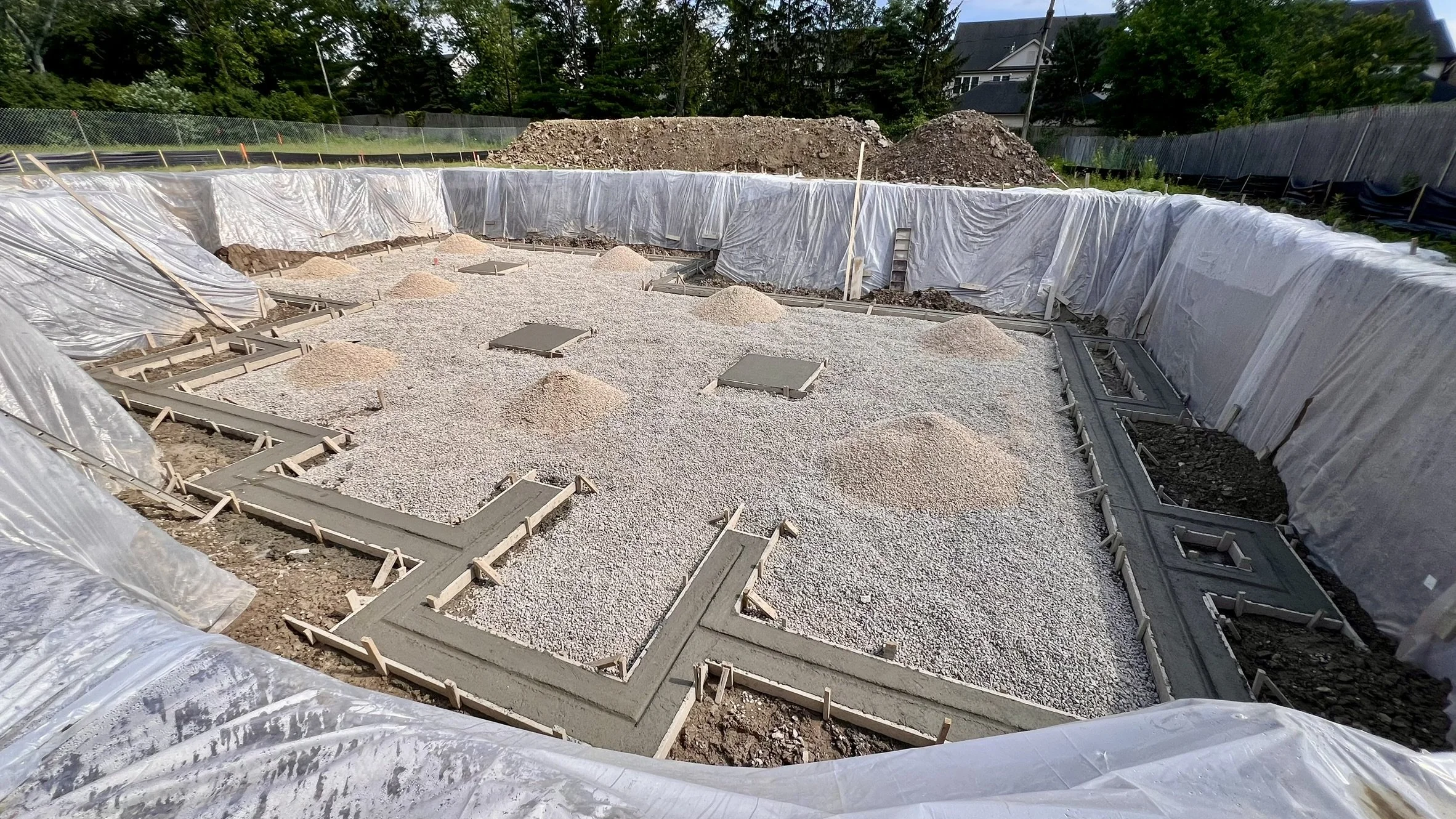 Coorlas Architecture new construction site showing a completed foundation with concrete and gravel, surrounded by plastic sheeting on the edges.