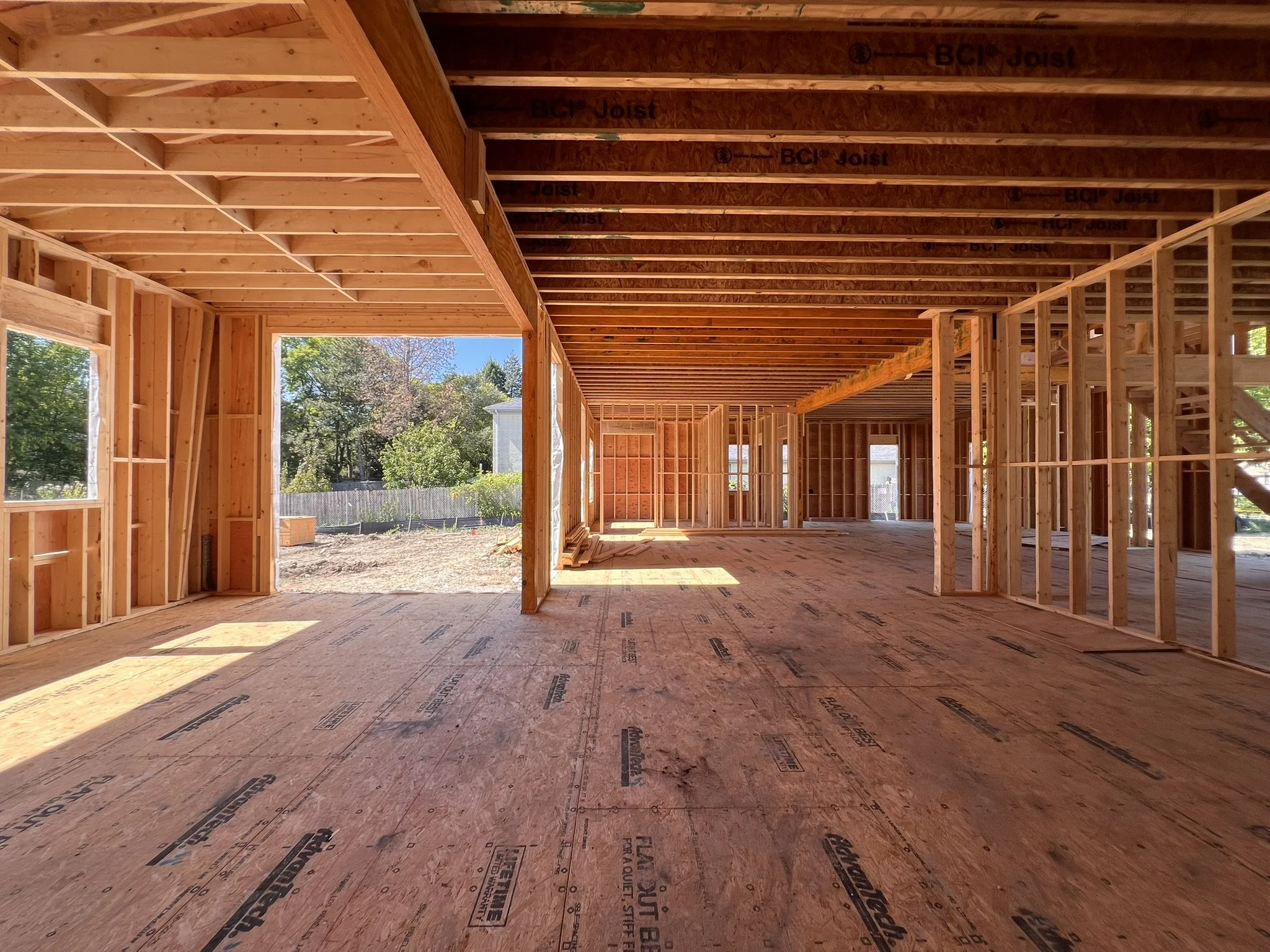 Coorlas Architecture luxury modern interior under construction with exposed wooden framing, stairs, large windows, and expansive tall spaces with long beam spans.