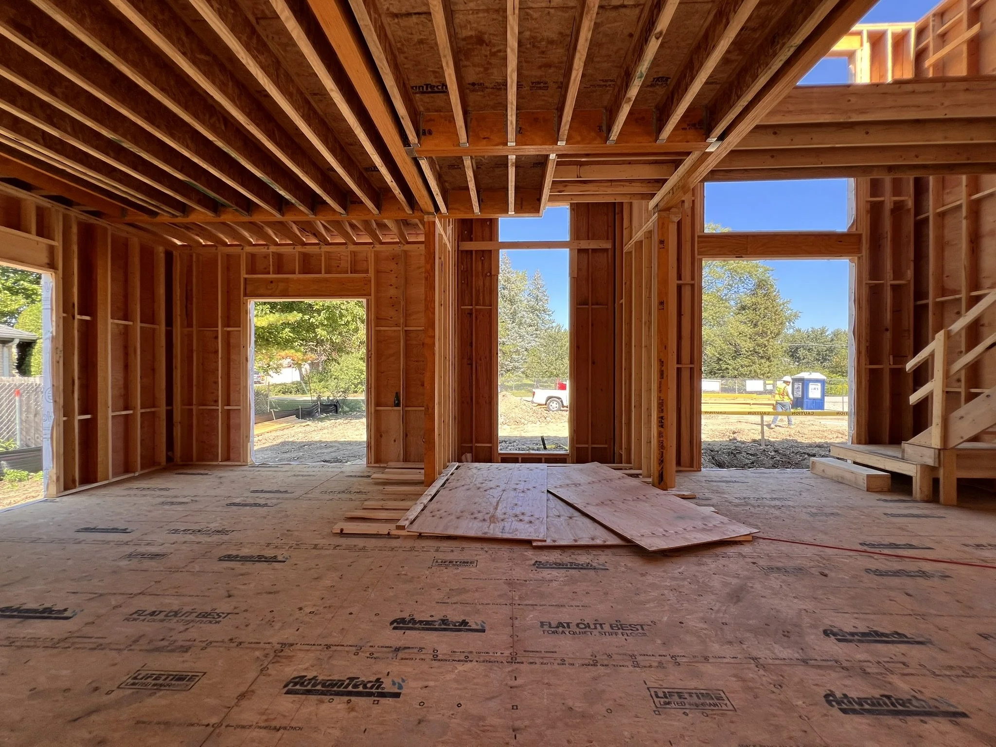Coorlas Architecture luxury modern interior under construction with exposed wooden framing, stairs, large windows, and expansive tall spaces with long beam spans.