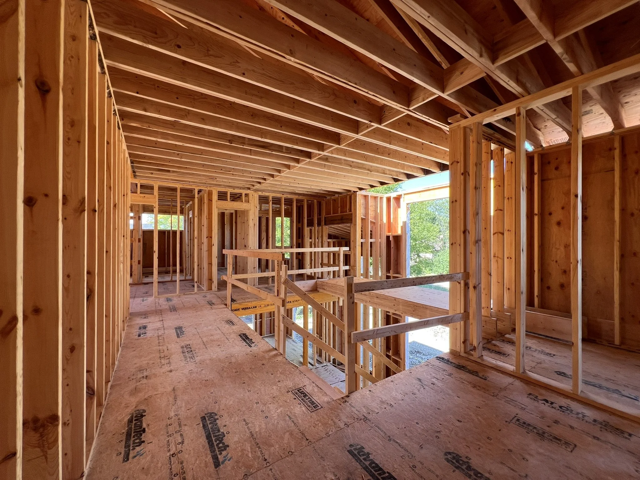 Coorlas Architecture luxury modern interior under construction with exposed wooden framing, stairs, large windows, and expansive tall spaces with long beam spans.