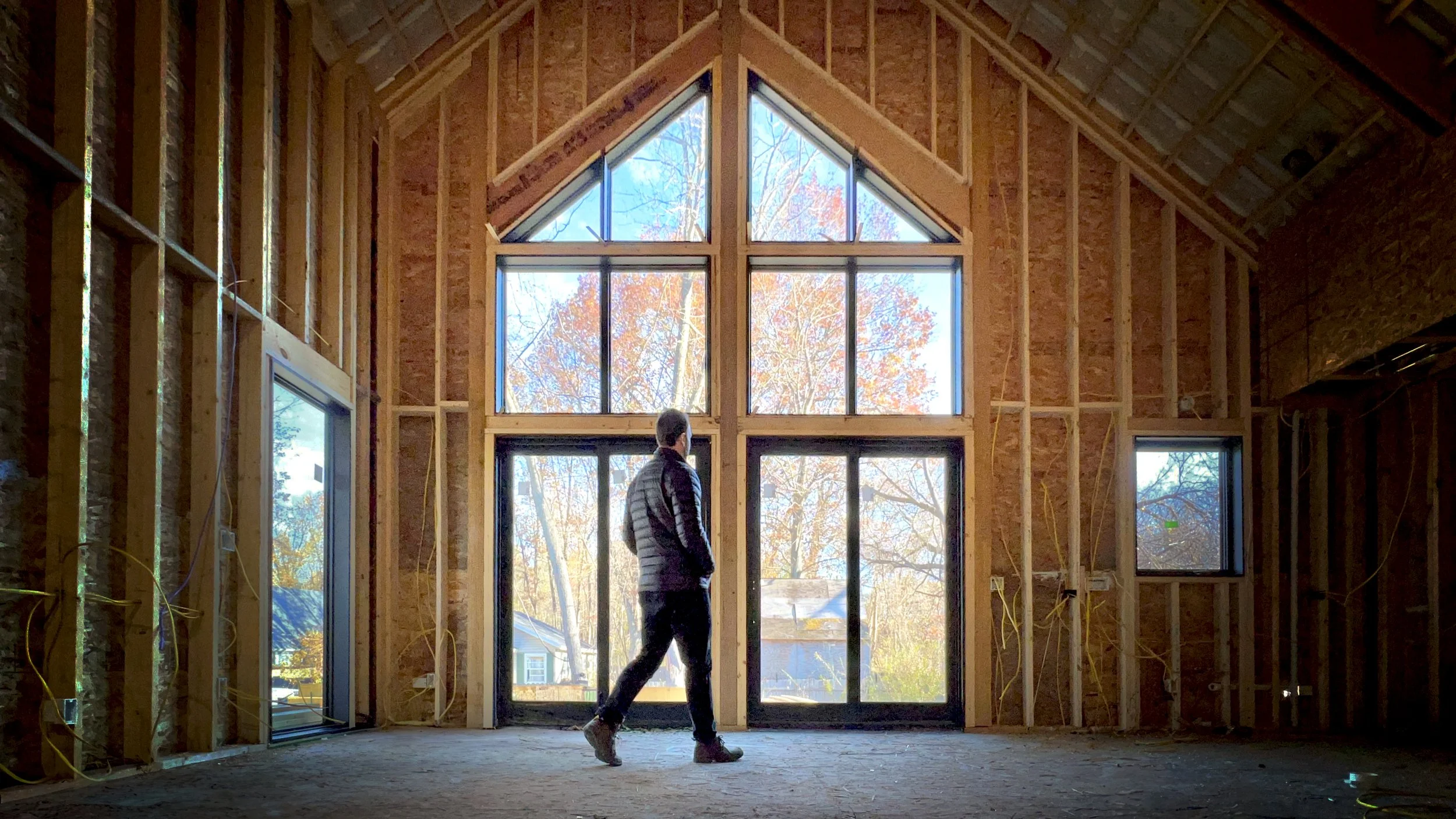 Coorlas Architecture modern farmhouse interior construction in Lakeside, Michigan. The interior features vaulted ceilings with exposed structural beams, and expansive full height window openings.