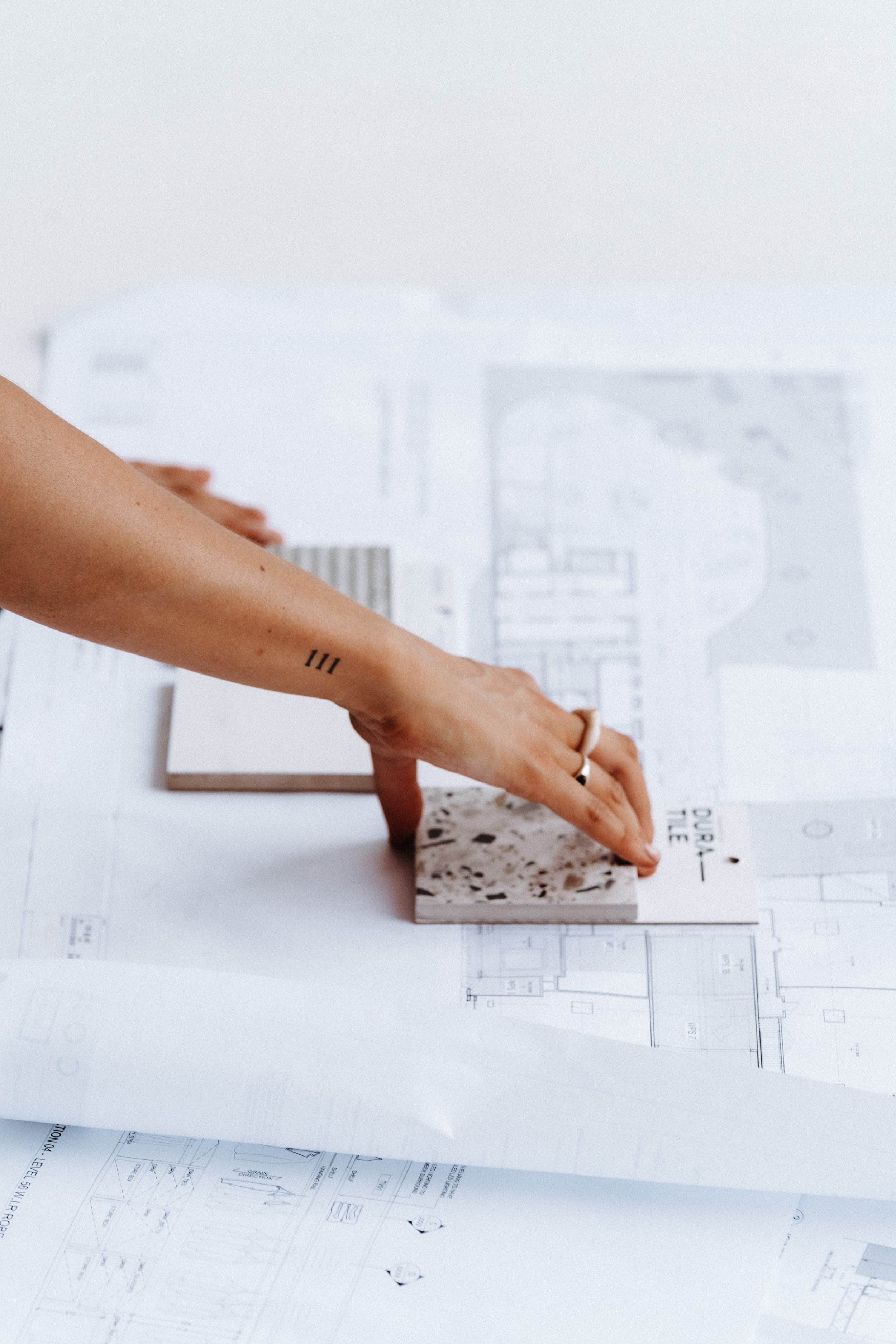 Architect hand placing a material sample on architectural plans during a design consultation melbourne