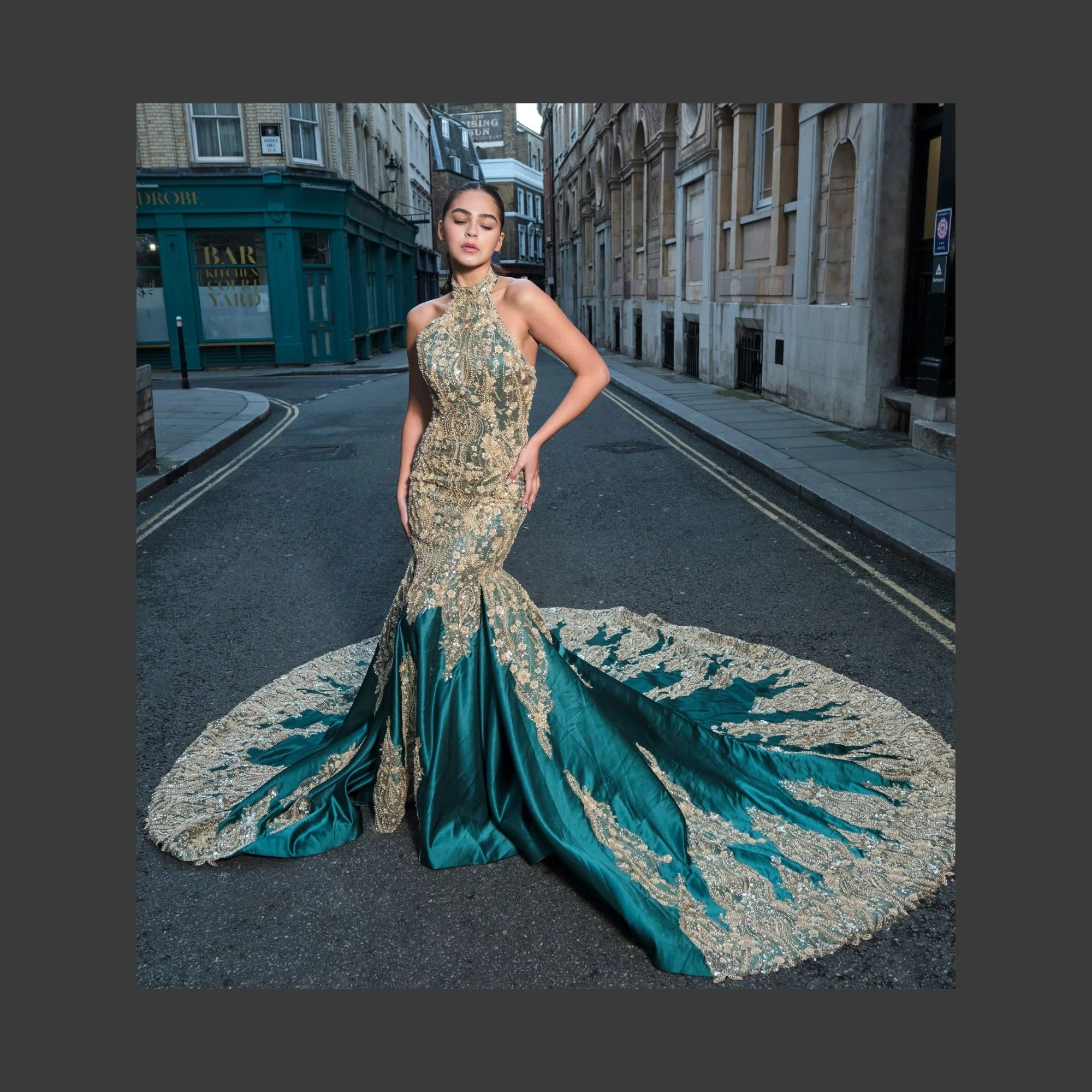 A woman in an ornate, embellished gown with a long train standing on a city street.
