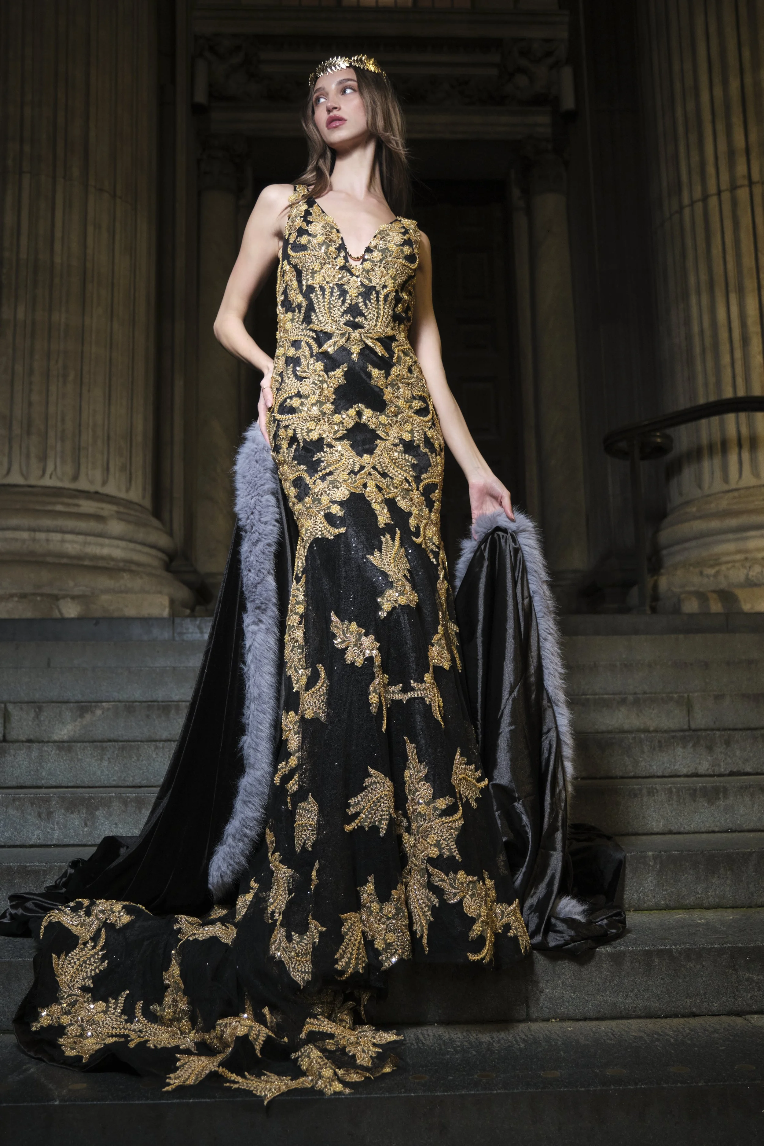 A woman standing against a light gray background, wearing black sunglasses, a multicolored furry coat, black pants, and black high-heeled boots.