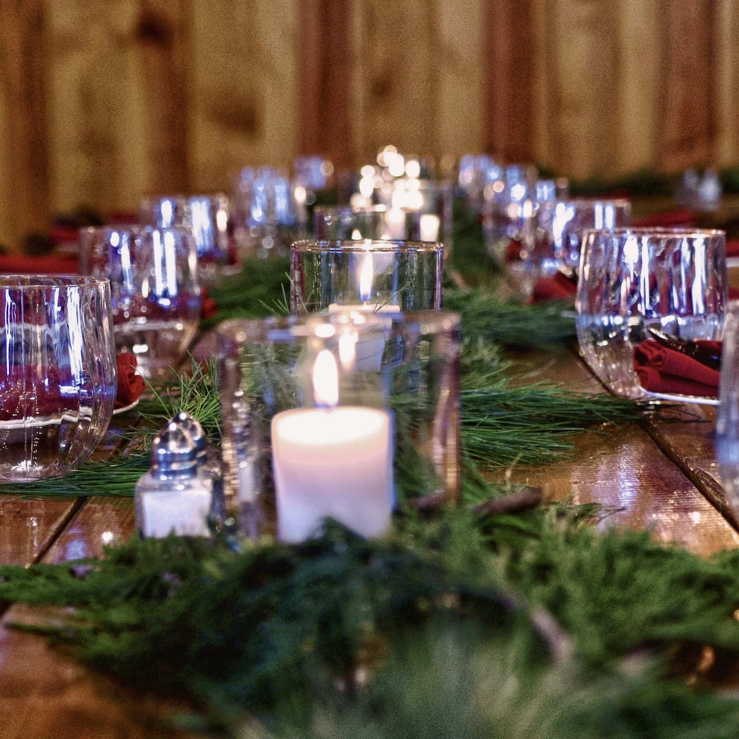 A decorated dining table with candles, glasses, and holiday greenery.