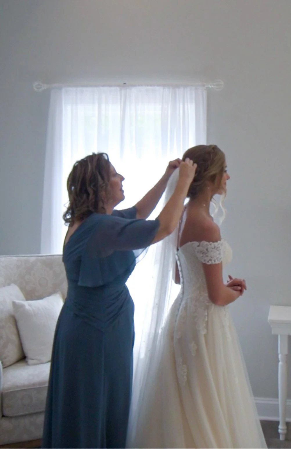 A woman helping a bride with her wedding dress before a wedding ceremony.