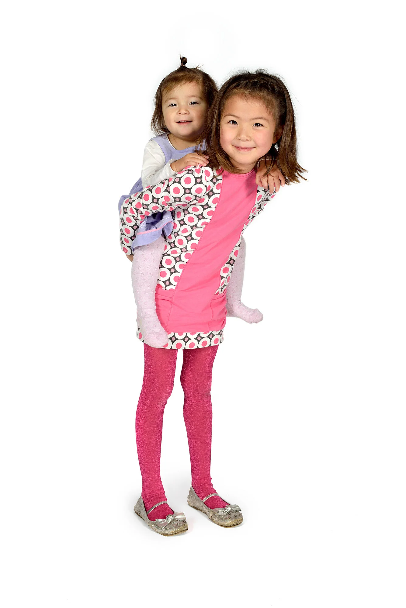 A girl gives her little sister a piggy back during a studio portrait session