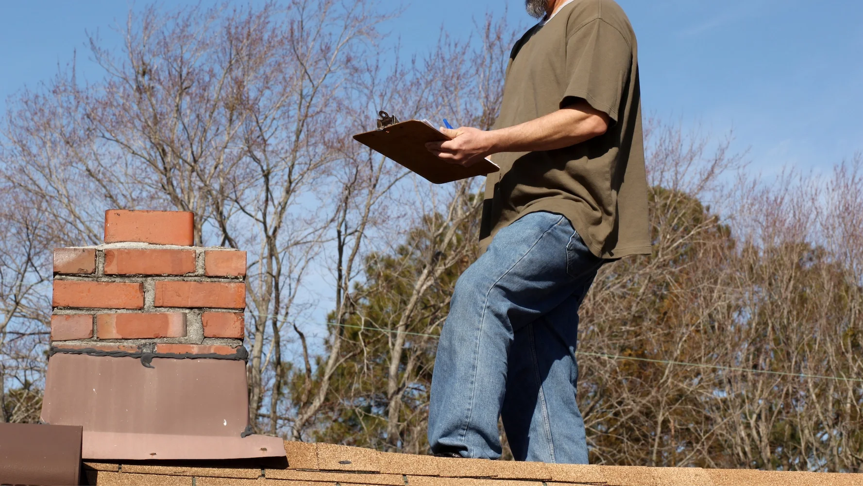 Sweeps N Ladders technician conducting a rooftop chimney inspection, noting findings on a clipboard beside a brick chimney in North Texas.
