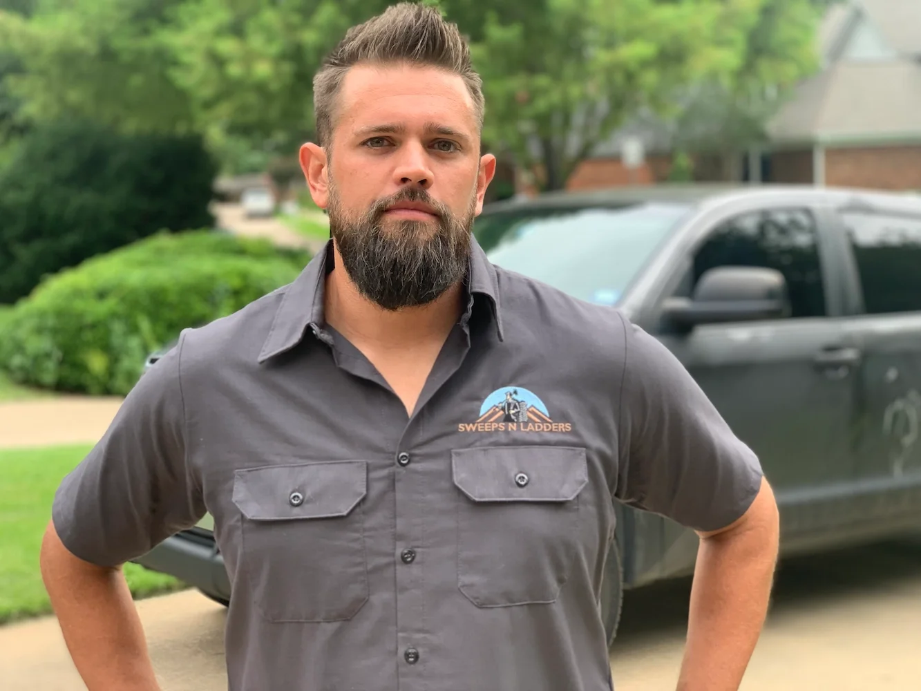A man with a beard wearing a gray shirt with a logo that reads 'Swipes N Ladders' standing outdoors next to a black pickup truck.