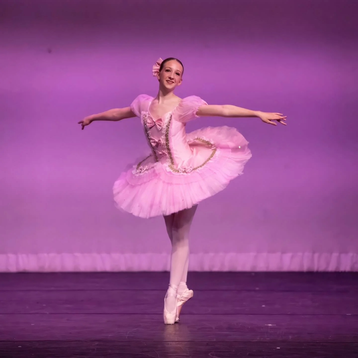 Ballet dancer in pink tutu on stage, performing a pose.
