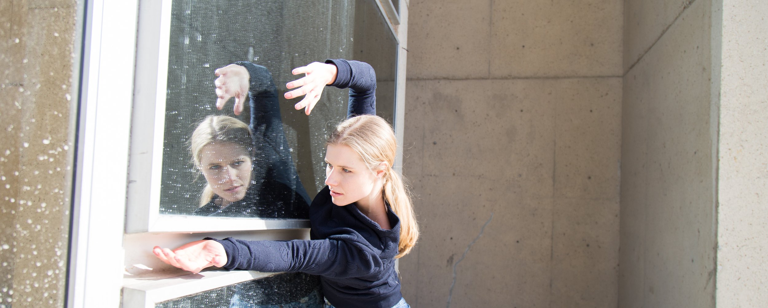 Woman posing artistically in front of a window with reflection, wearing a navy sweater.
