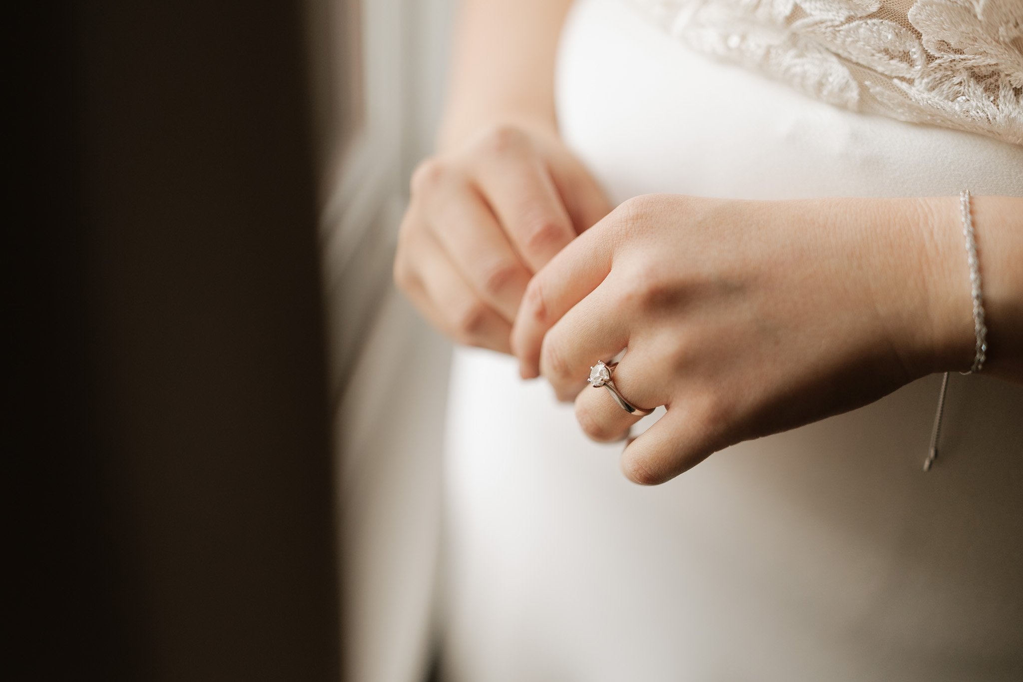Close-up of a woman wearing a wedding dress, holding a hand with a diamond engagement ring, and a delicate bracelet on her wrist.