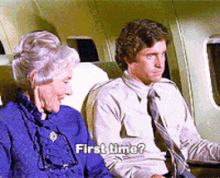 A young man and an older woman sitting next to each other on an airplane, with the woman speaking and the young man looking at her, asking, "First time?"